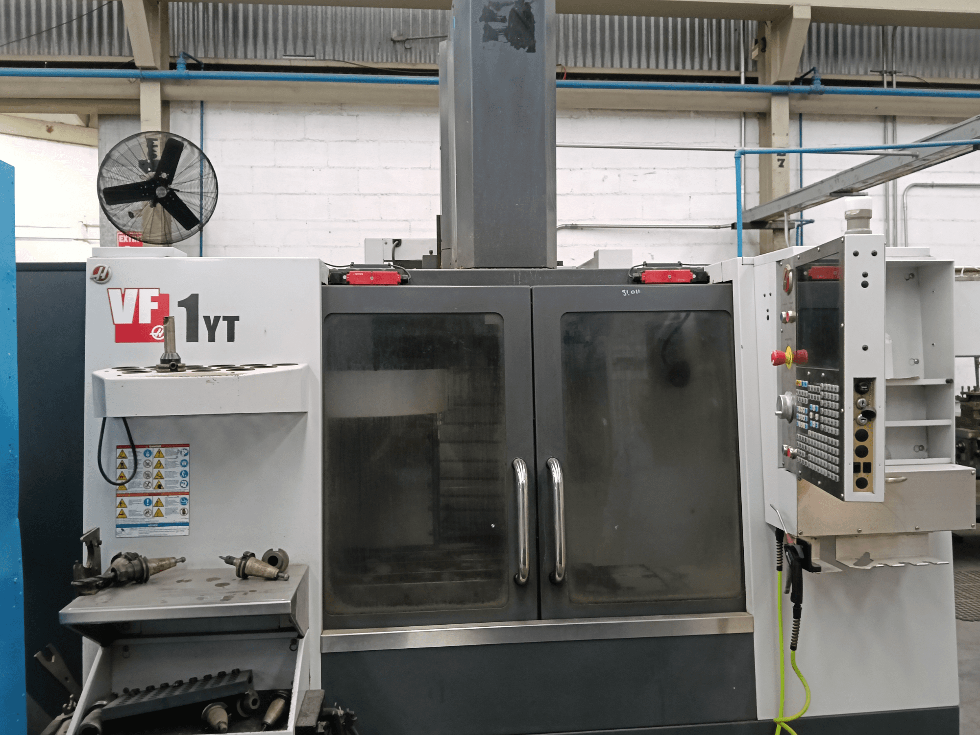 Vue de face du centre d'usinage vertical HAAS VF-1YT-1, avec le panneau de commande et les outils sur le côté.