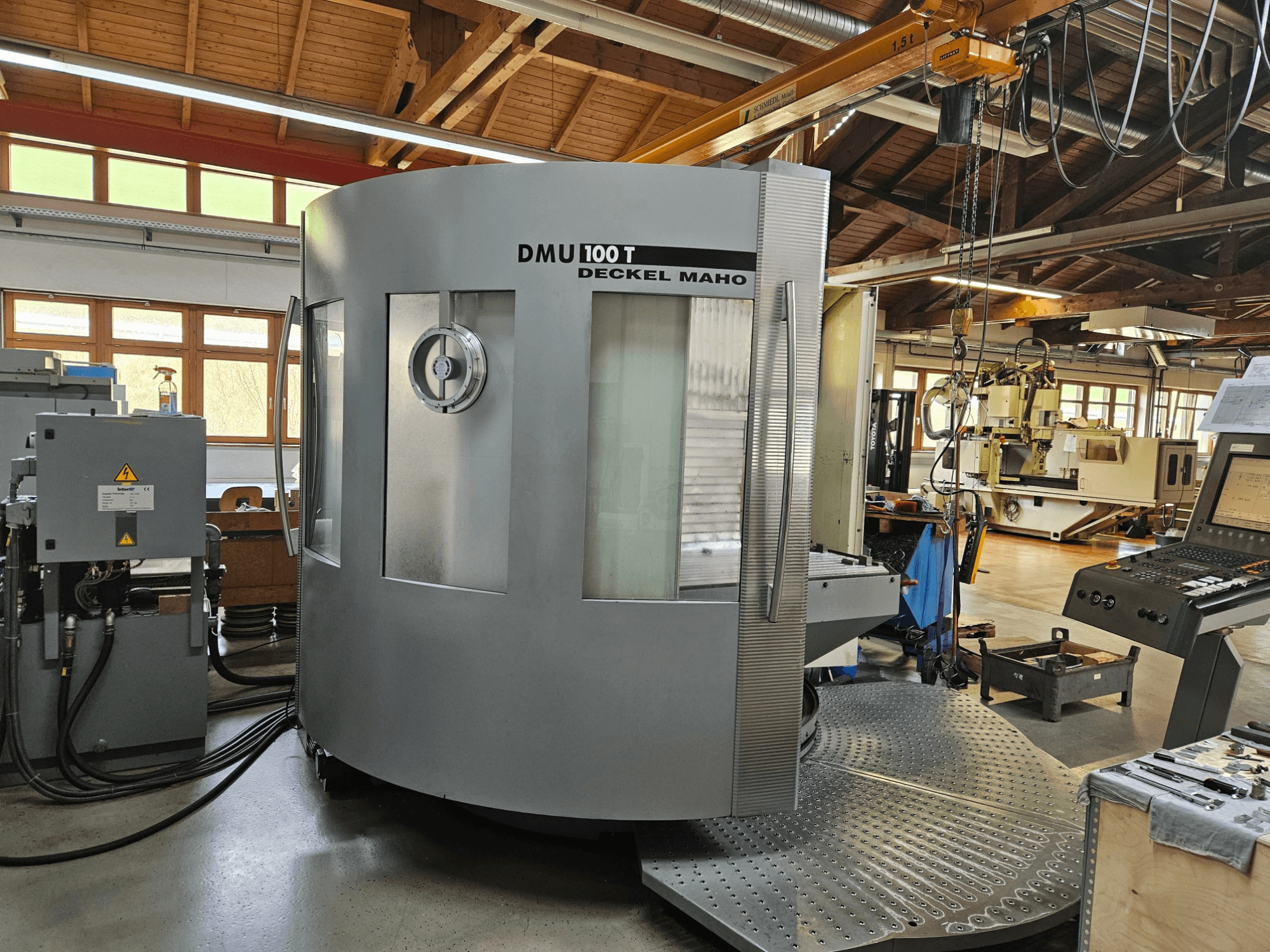 Machine CNC DMU 100 T Deckel Maho vue de face, avec une grande base circulaire, un panneau de commande et un boîtier en verre.