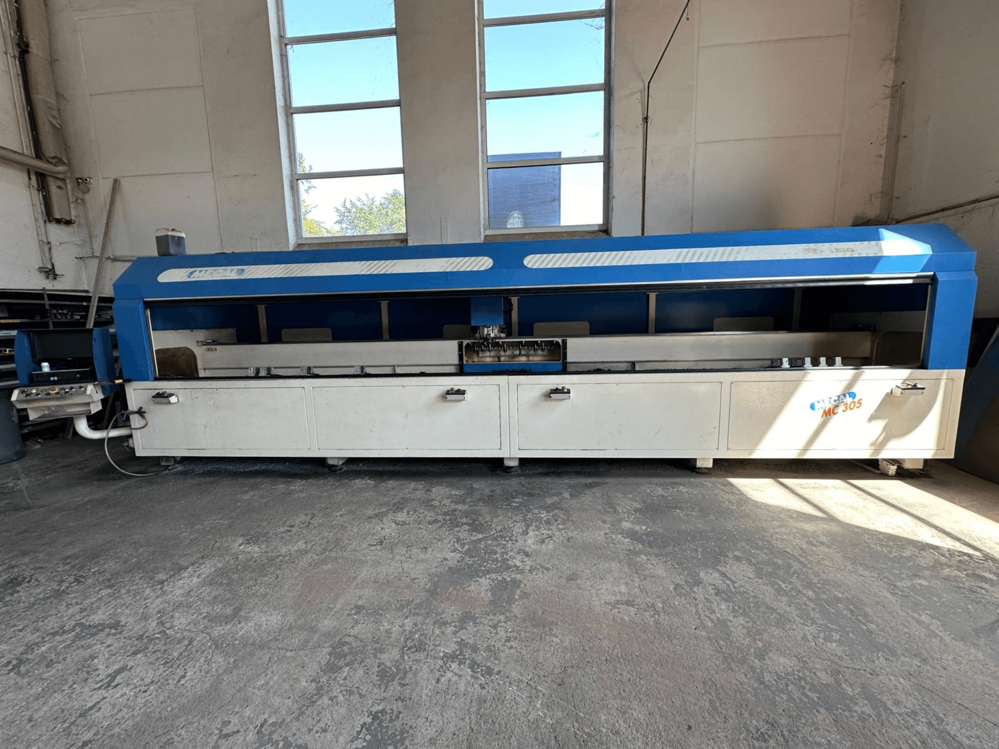 Vue avant du centre d'usinage vertical MECAL MC 305, avec un design bleu et blanc, une table de travail visible et un panneau de commande.