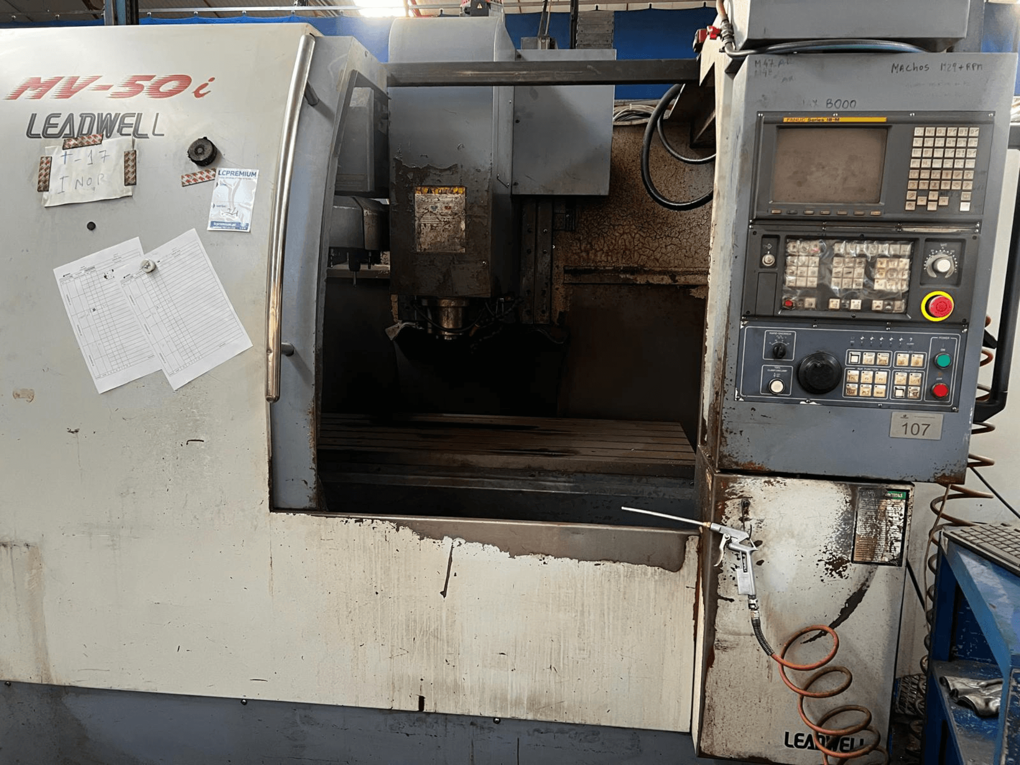 Centre d'usinage vertical Leadwell MV-50i, vue de face, montrant le panneau de commande, la zone de la broche et la table de travail présentant des traces d'usure.