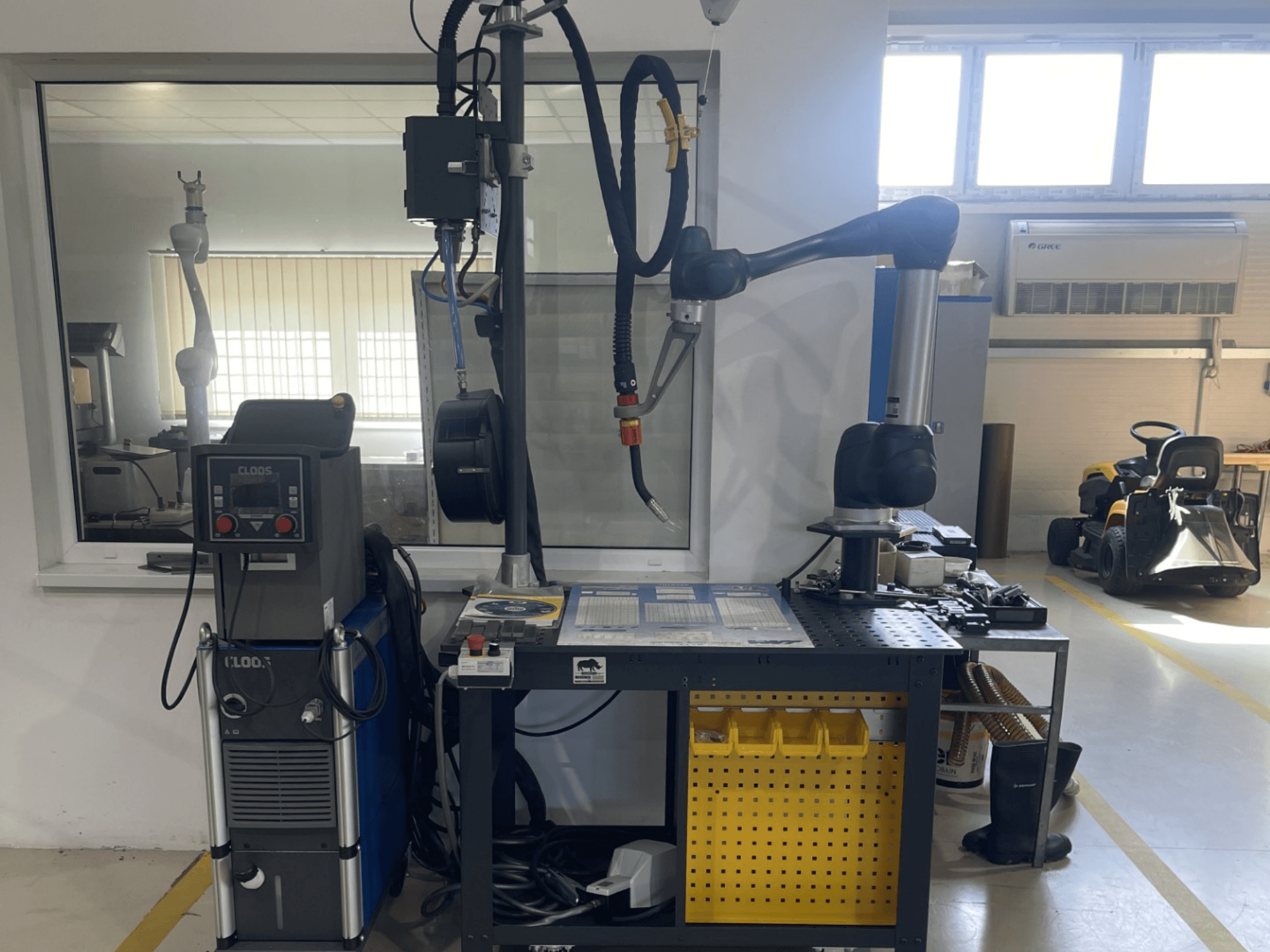Robot collaboratif DOOSAN M1013 dans un atelier, vue de profil avec du matériel de soudure et des outils posés sur un établi.