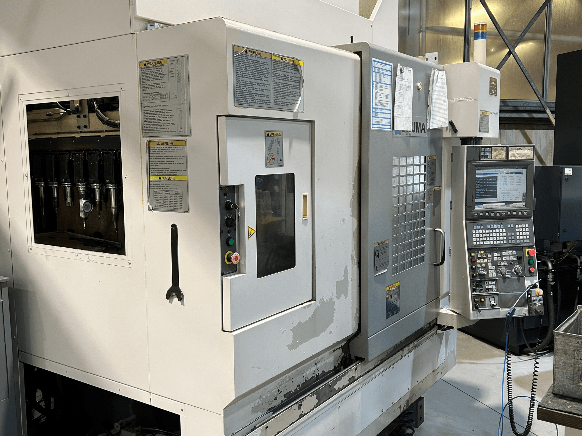 Vue de face d'une machine CNC UMA avec les porte-outils visibles, le panneau de commande, les étiquettes d'avertissement et les boutons de commande.