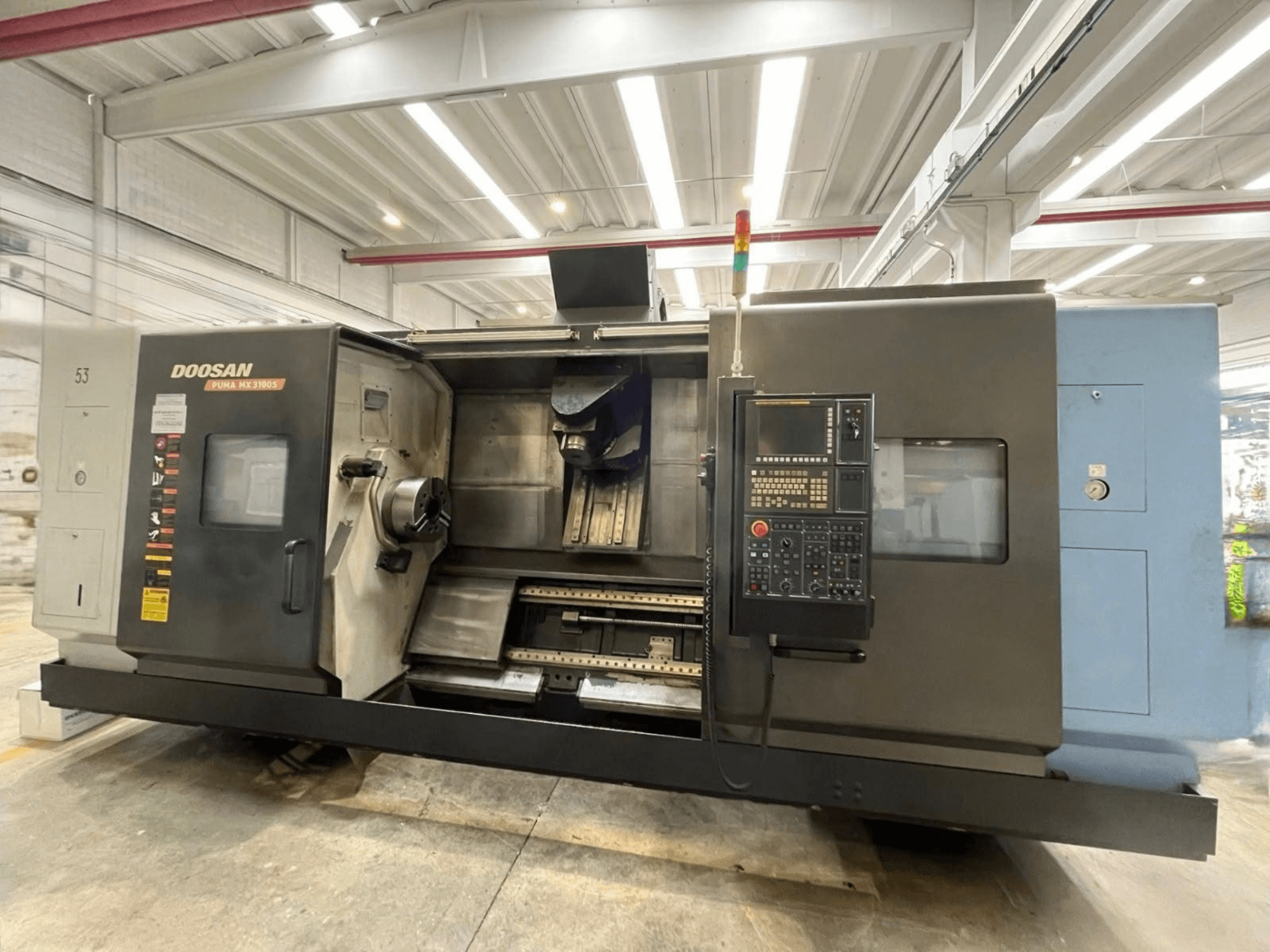 Vue de face d'un tour horizontal DOOSAN PUMA MX3100, avec le panneau de commande ainsi que la broche et la zone de fixation des outils bien visibles.
