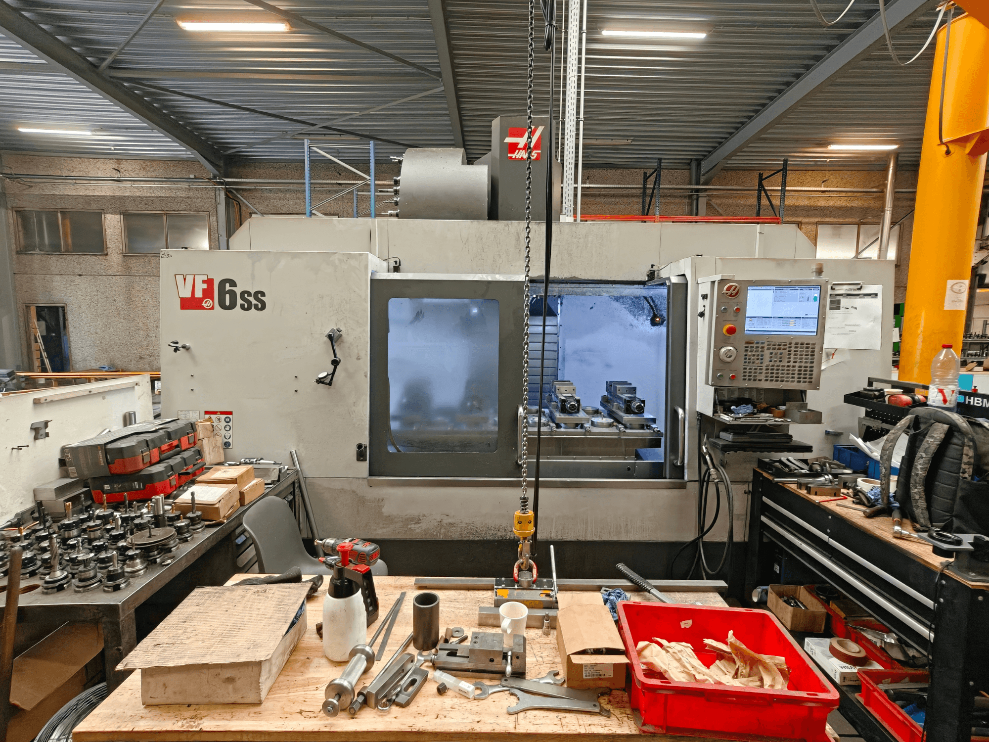 Centre d'usinage vertical Haas VF-6SS dans un atelier, vue de profil montrant le panneau de commande et l'espace de travail encombré d'outils.