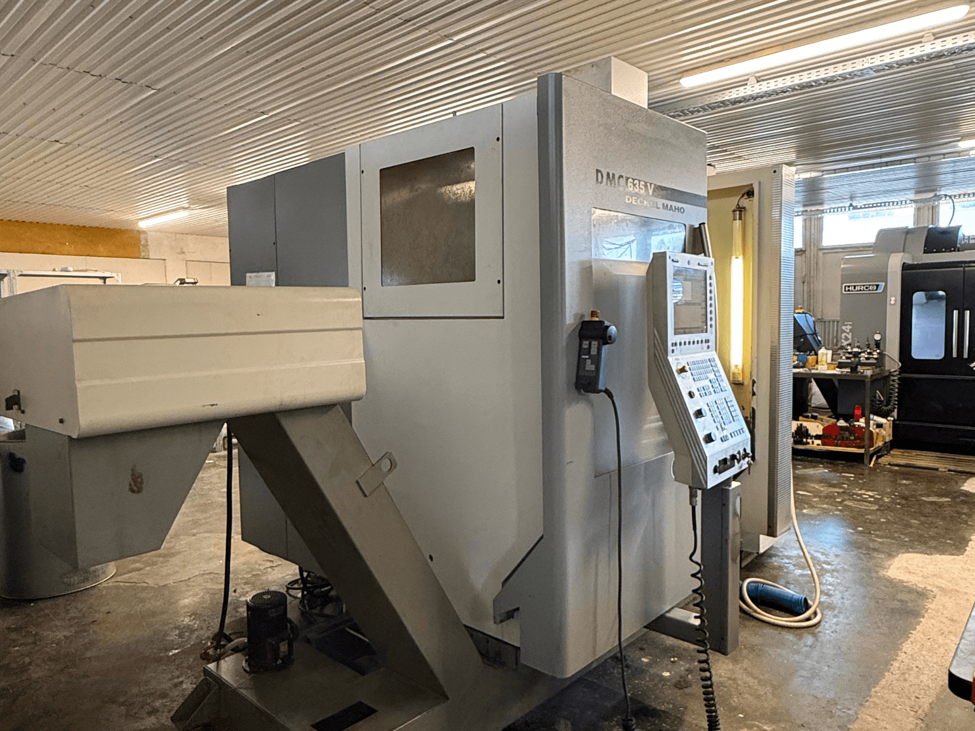 Fraiseuse DMC G635V dans un atelier, vue de face avec le panneau de commande et les outils électriques connectés visibles.