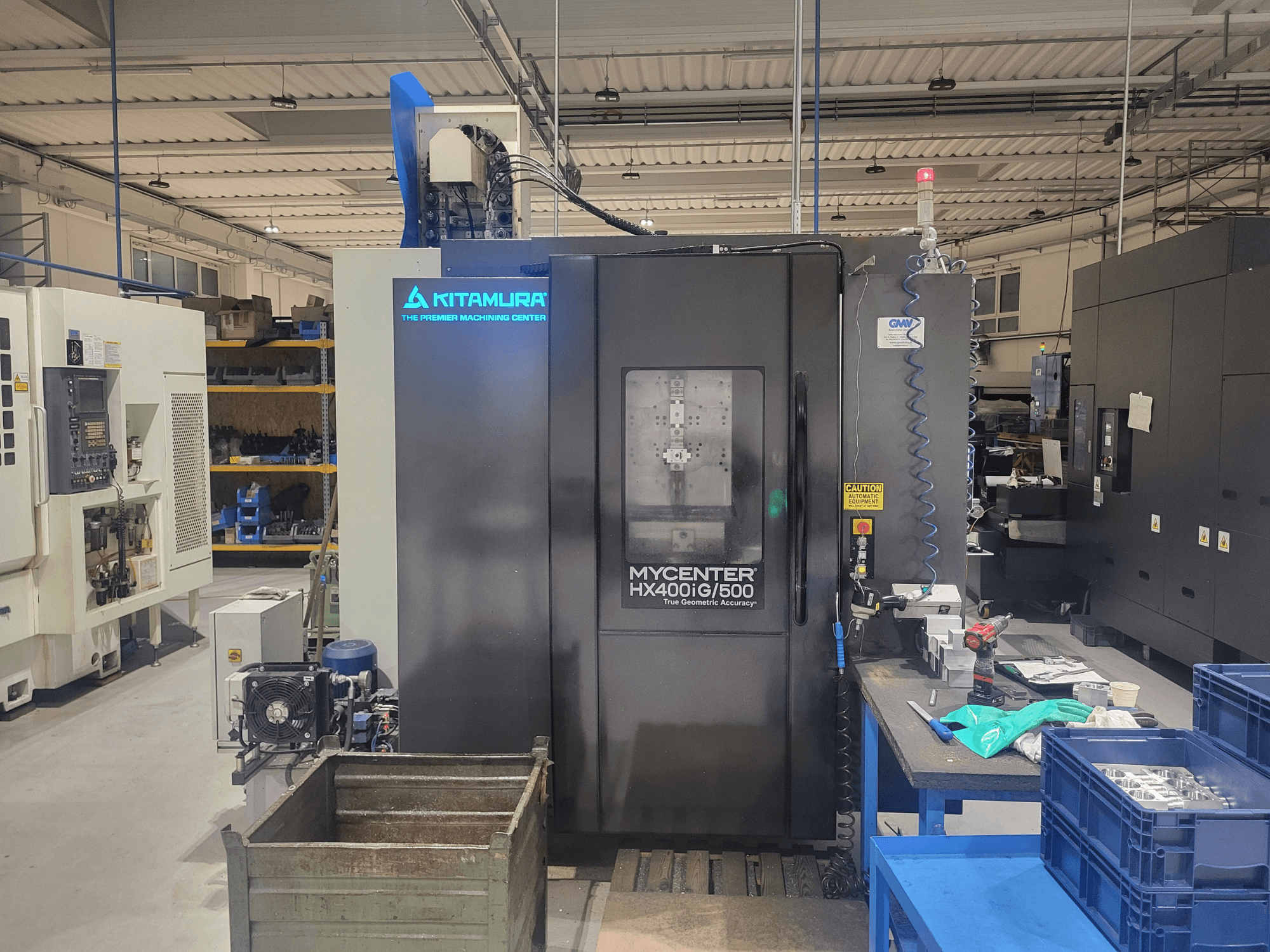 Machine CNC Kitamura Mycenter HX400iG/500 dans un atelier, vue de face, avec les commandes, le stockage des outils et les matériaux à proximité.
