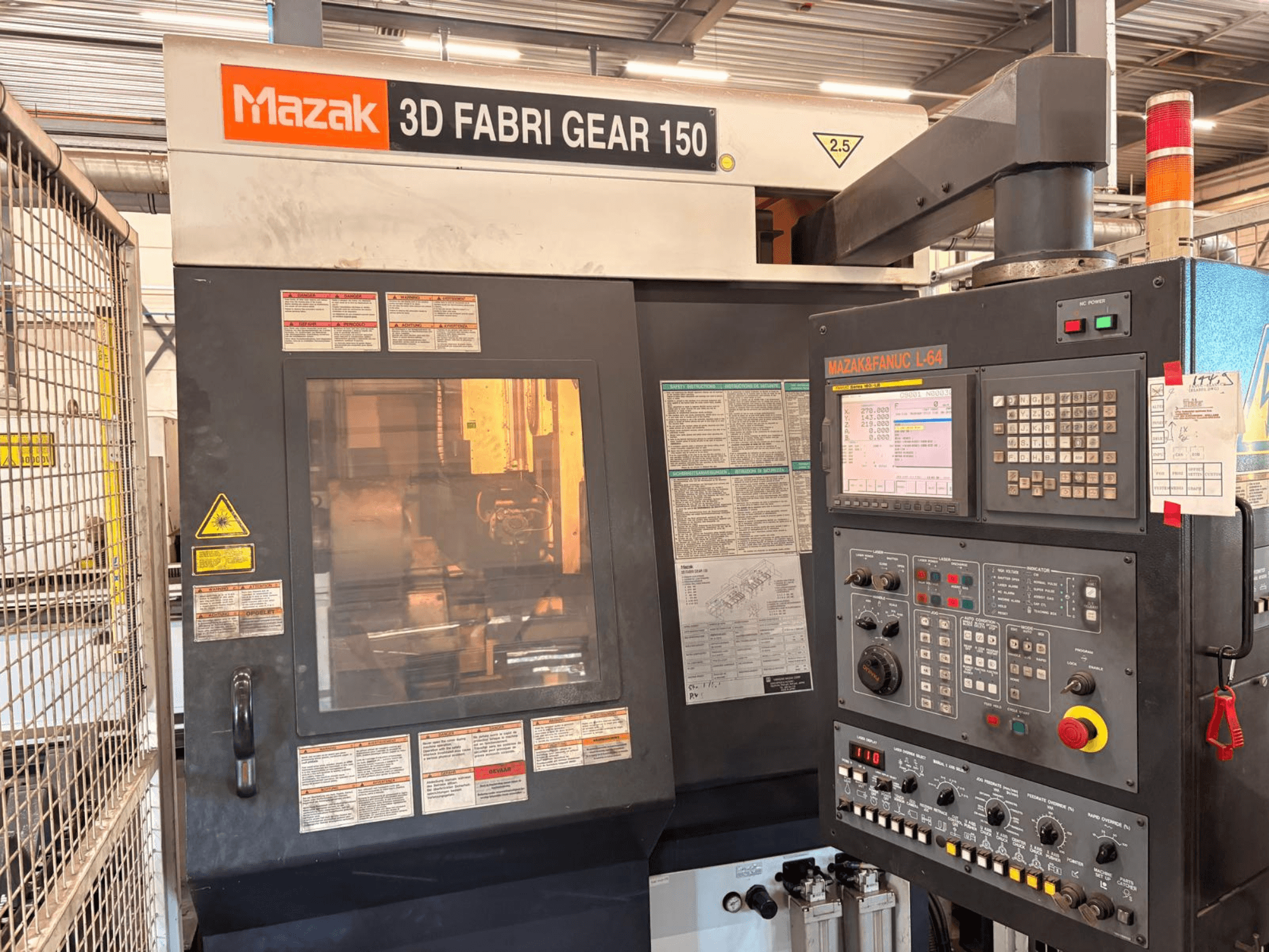 Machine de découpe de tubes Mazak 3D Fabri Gear 150, vue de face montrant le panneau de commande, les étiquettes de sécurité et l'interface utilisateur.