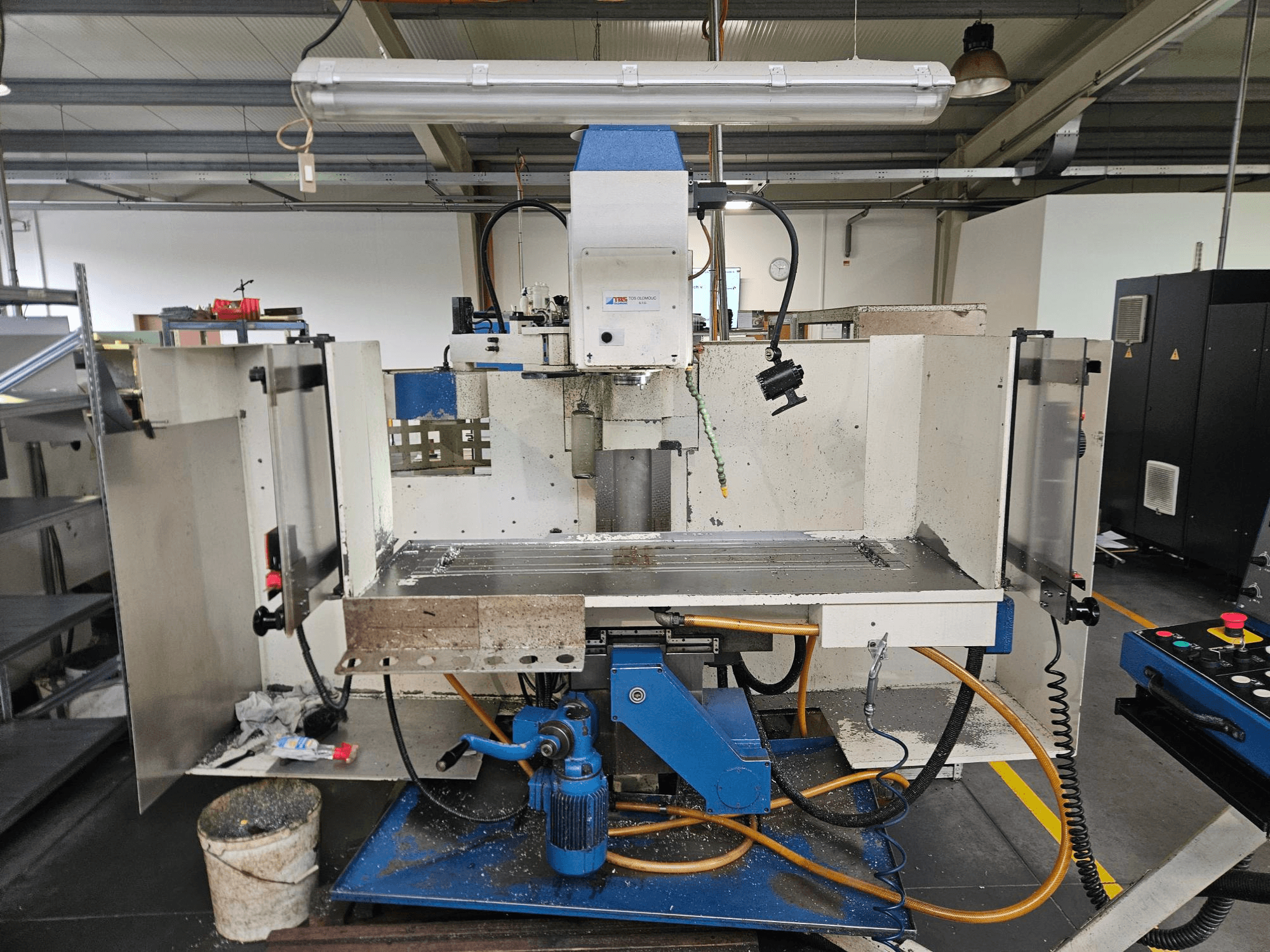 TOS Olomouc FV30 CNC Centre d'usinage vertical dans un atelier, vue de face montrant le panneau de commande, la table de travail et le système d'arrosage.