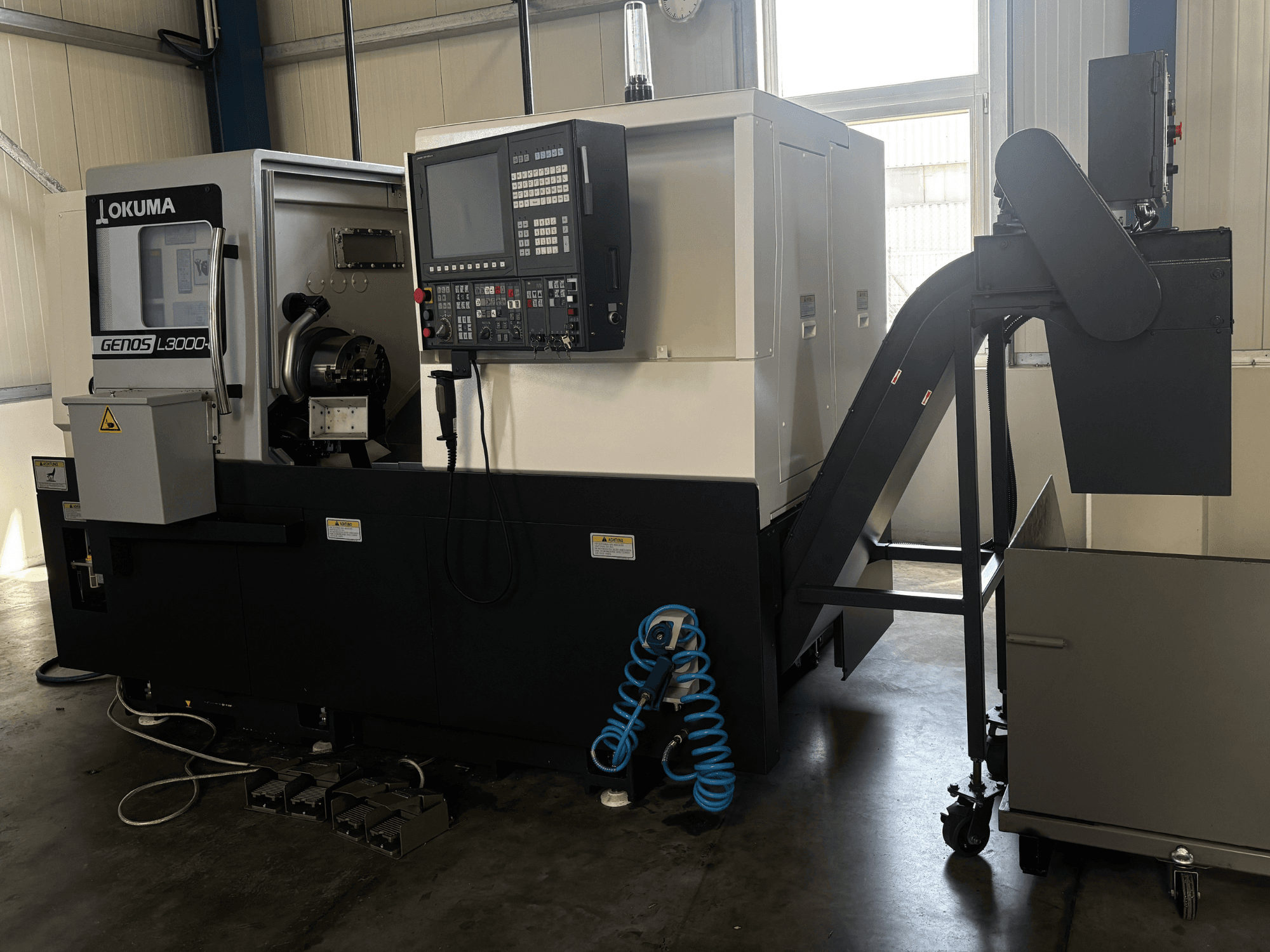 Tour horizontal Okuma GENOS L3000-e, vue de face, présentant le panneau de commande, le convoyeur et la zone de la broche.