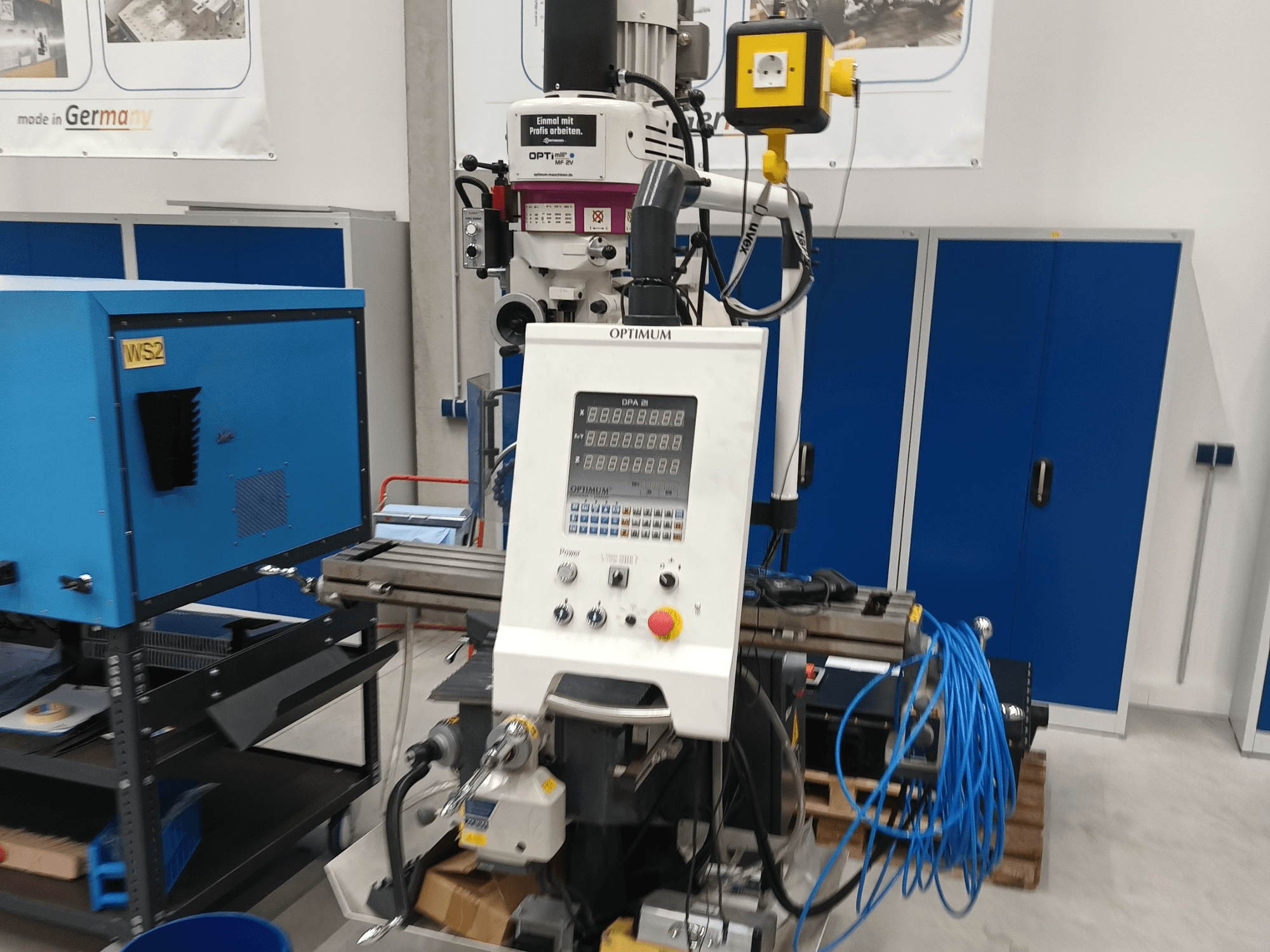 Centre d'usinage vertical Optimum OPTImill MF 2V, vue de face montrant le panneau de commande, la broche et le chariot de support bleu.