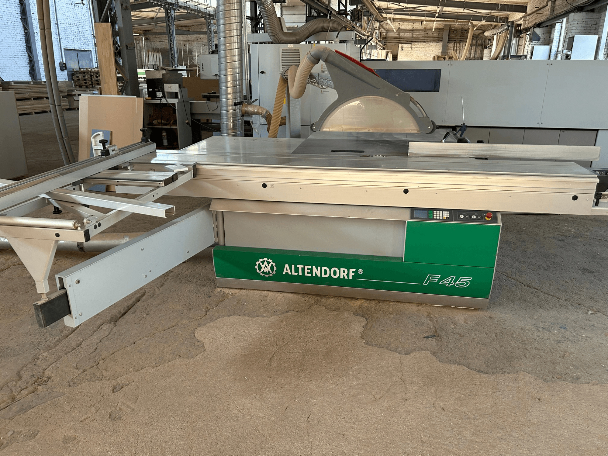 Scie à panneaux Altendorf F 45, vue de face, montrant la table de coupe, le carter de protection de la lame et le panneau de commande sur la machine verte et grise.