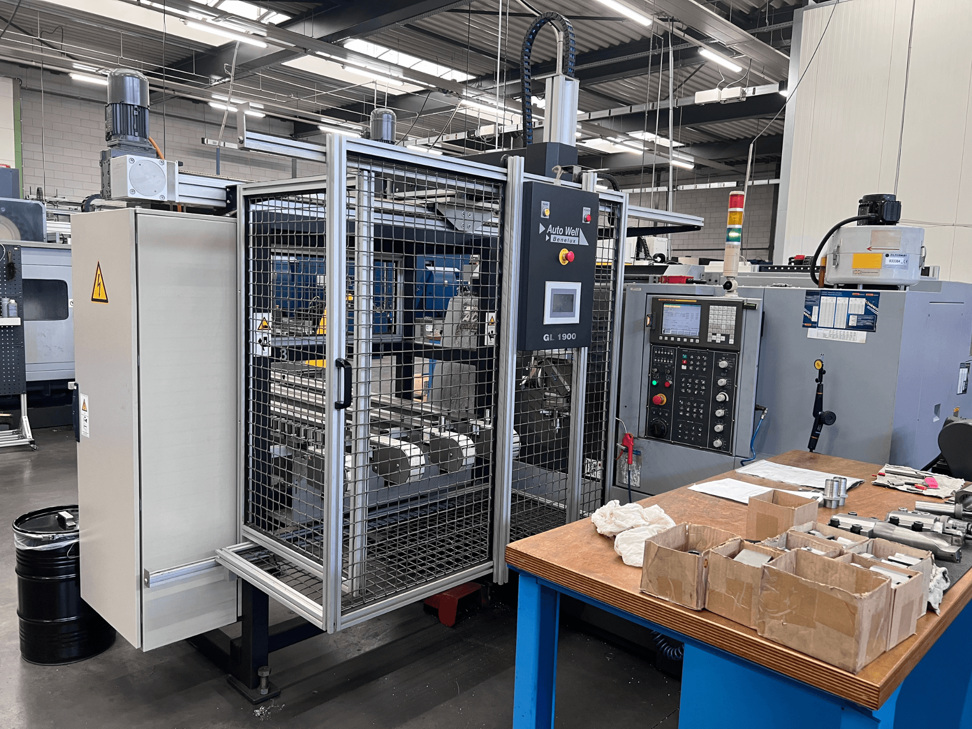 Vue de face de la machine Auto Weld GL 1900 avec le panneau de commande, l'enceinte de sécurité et les outils environnants sur un établi.