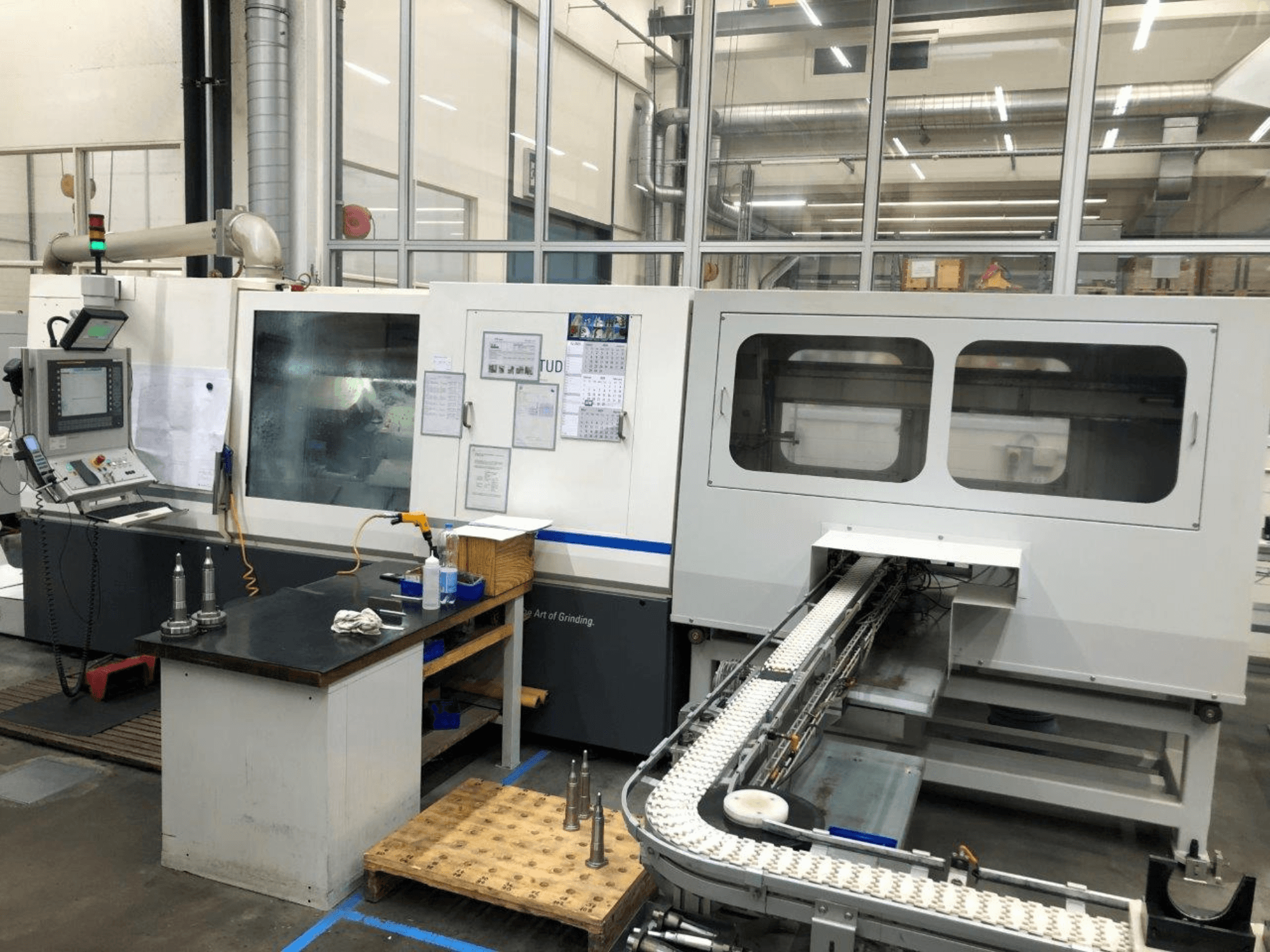 Meuleuse CNC avec panneau de commande, vue de face ; comporte un convoyeur et des fenêtres de visualisation claires, mettant en valeur les outils de précision.