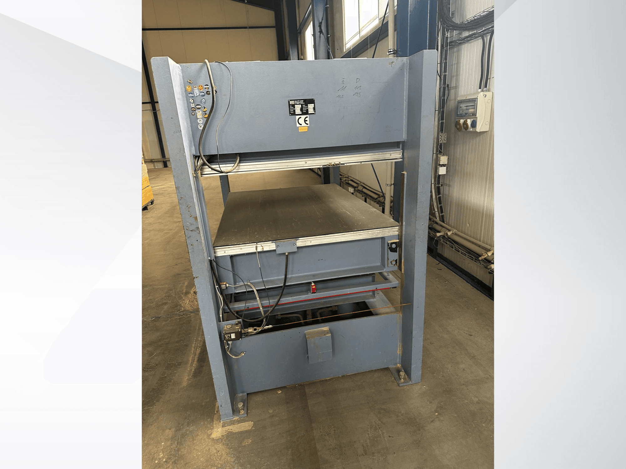 Machine industrielle grise avec panneau de commande, vue de face ; comprend des plates-formes réglables et des marquages de sécurité.