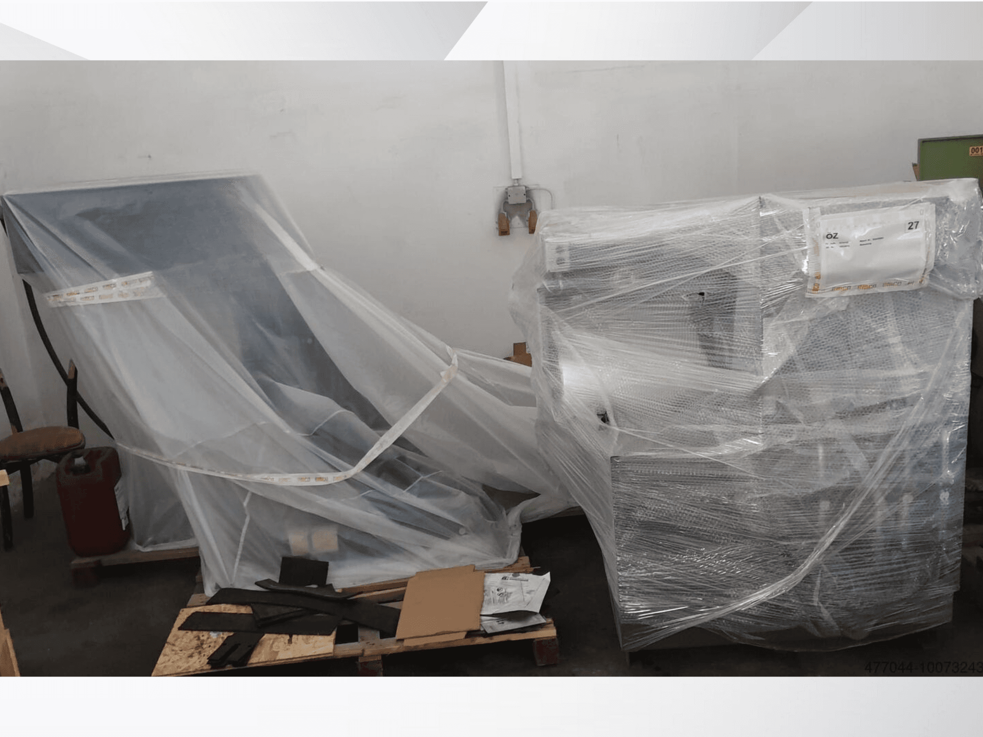 Équipement industriel emballé dans du plastique, comprenant une chaise et une machine, vu d'un angle latéral dans un entrepôt.