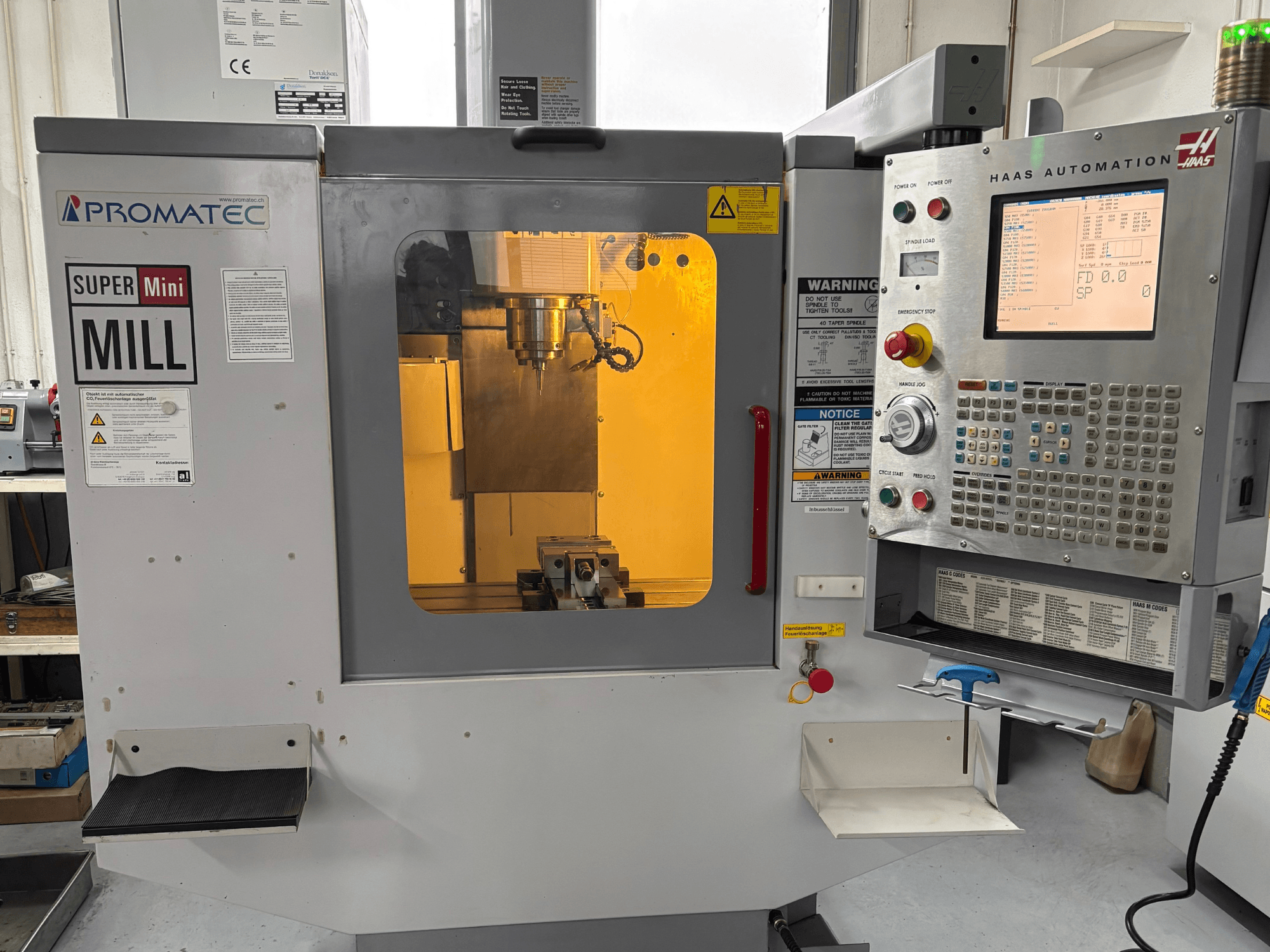 Promatec Super Mini Mill en vue de face, équipé d'un panneau de commande Haas Automation et d'un outil de coupe visible à l'intérieur.