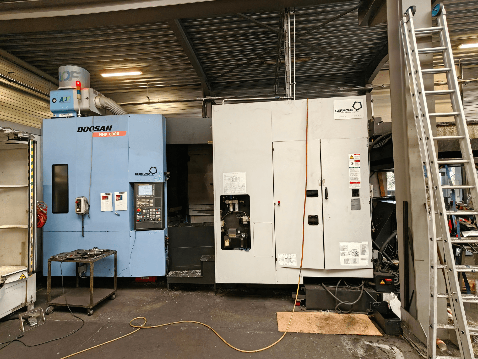 Vue de face du centre d'usinage horizontal DOOSAN NHP6300, mettant en évidence le panneau de commande et les machines adjacentes dans un atelier.