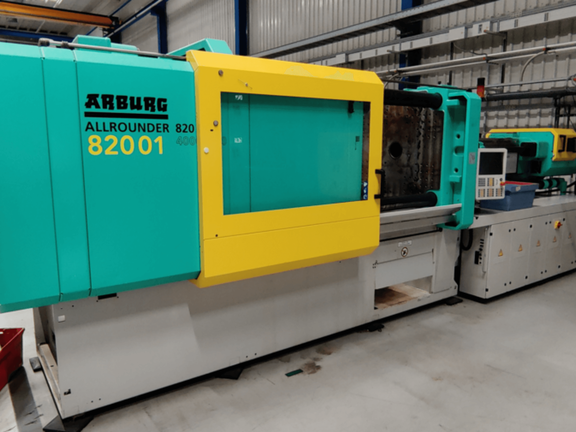 Machine de moulage par injection Arburg ALLROUNDER 82001 de couleur sarcelle et jaune, vue de côté montrant le panneau de commande et les caractéristiques opérationnelles.