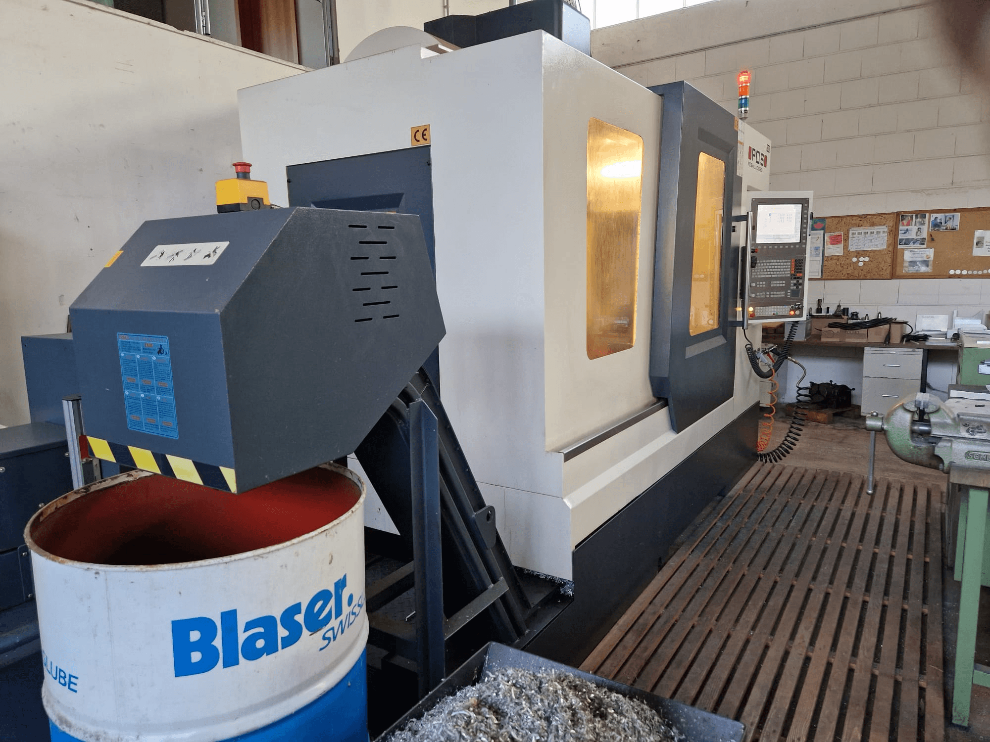 Vue avant du centre d'usinage vertical POSmill C 1050, avec le système d'arrosage au-dessus du tambour Blaser et le panneau de commande visible.