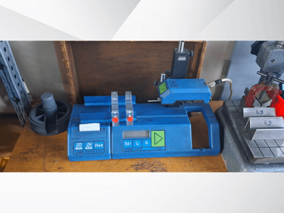 Imprimante Hommel T 1000 bleue et testeur T 1 010 avec boutons rouges, vus de face sur un établi avec des blocs métalliques.