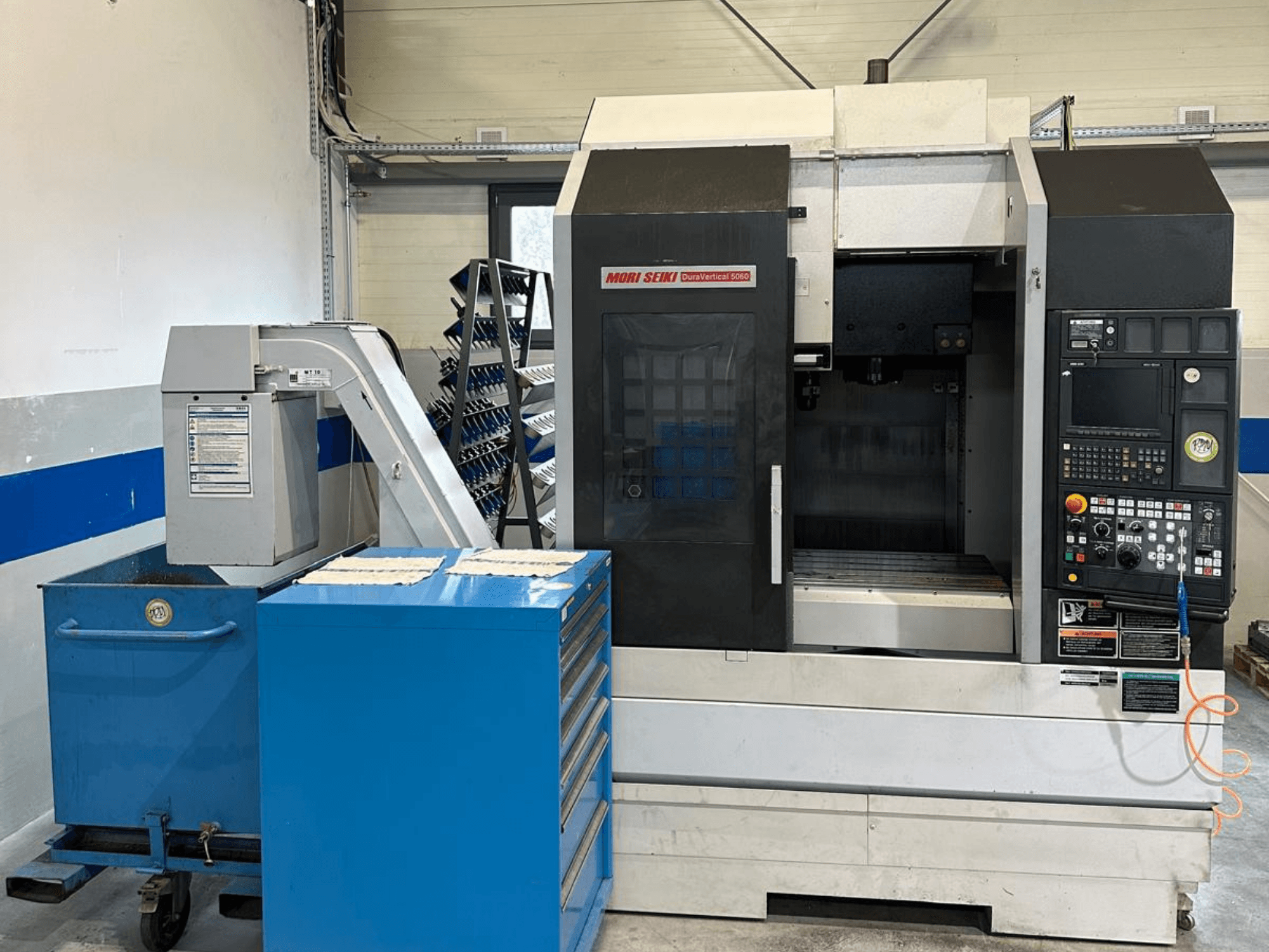 MORI SEIKI DURA VERTICAL 5060, vue de face d'un centre d'usinage vertical avec son panneau de commande et son magasin d'outils situé à proximité.
