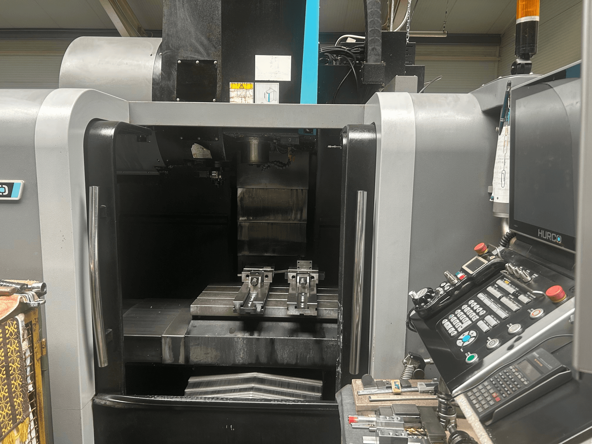 Vue de face du centre d'usinage CNC Hurco, montrant le porte-outil, la pièce métallique et le panneau de commande avec les boutons et l'écran.