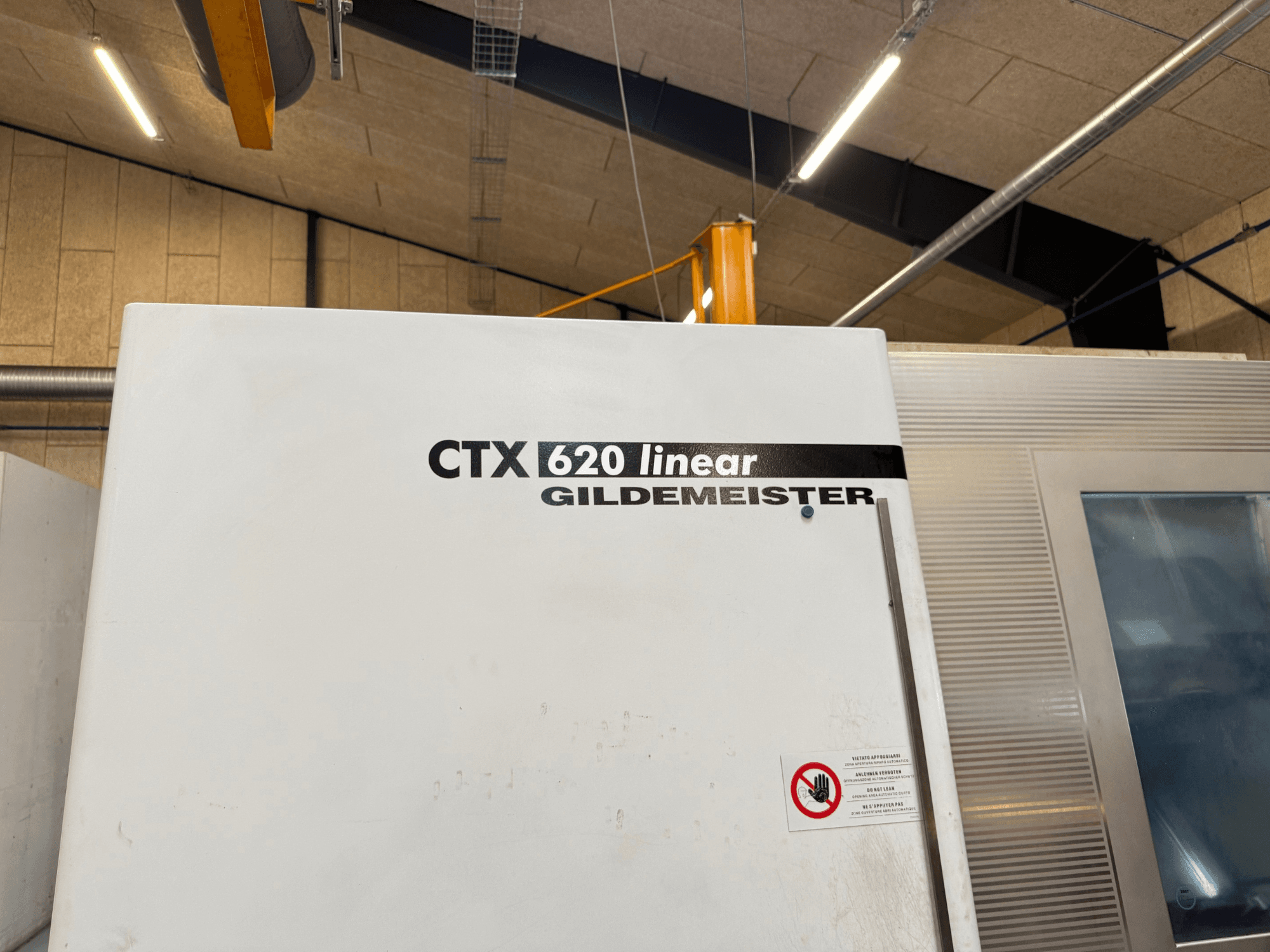 Vue latérale de la machine CTX 620 Linear Gildemeister, avec un extérieur blanc et des étiquettes d'avertissement de sécurité.