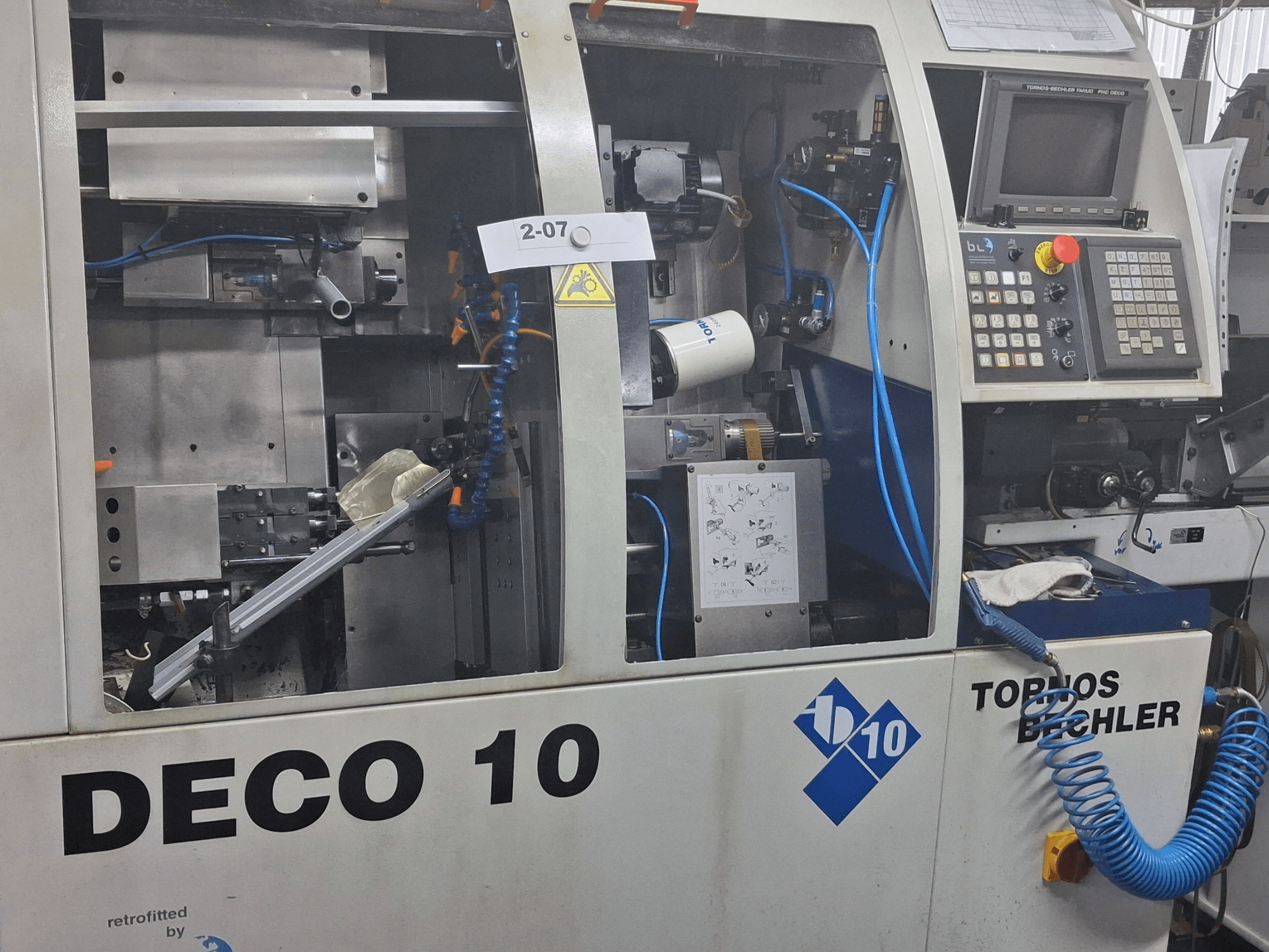 Vue rapprochée de la machine de tournage TORNOS Deco 10a de type suisse, montrant les détails du mécanisme interne et du panneau de commande.