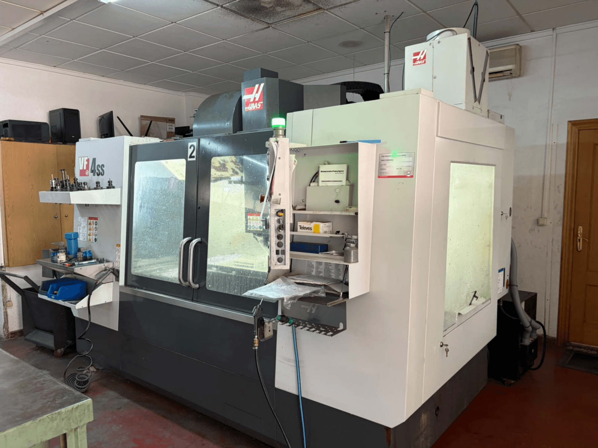 Centre d'usinage vertical HAAS VF 4SS dans un atelier, vue de face, montrant le panneau de commande et la zone de travail avec les outils et les matériaux.
