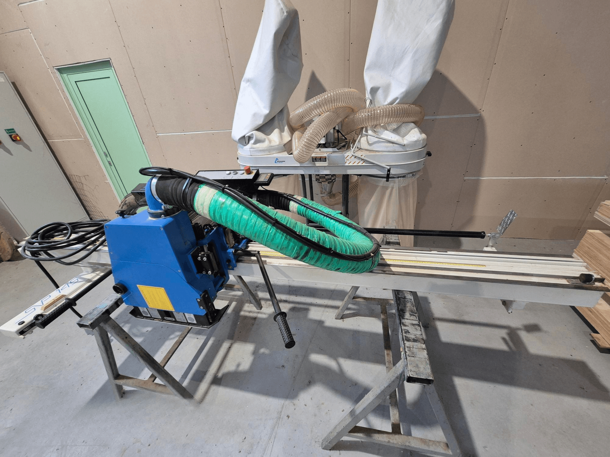 Scie à panneaux horizontale SVP-175 bleue avec support et tuyau à poussière verts, vue de côté dans un atelier.