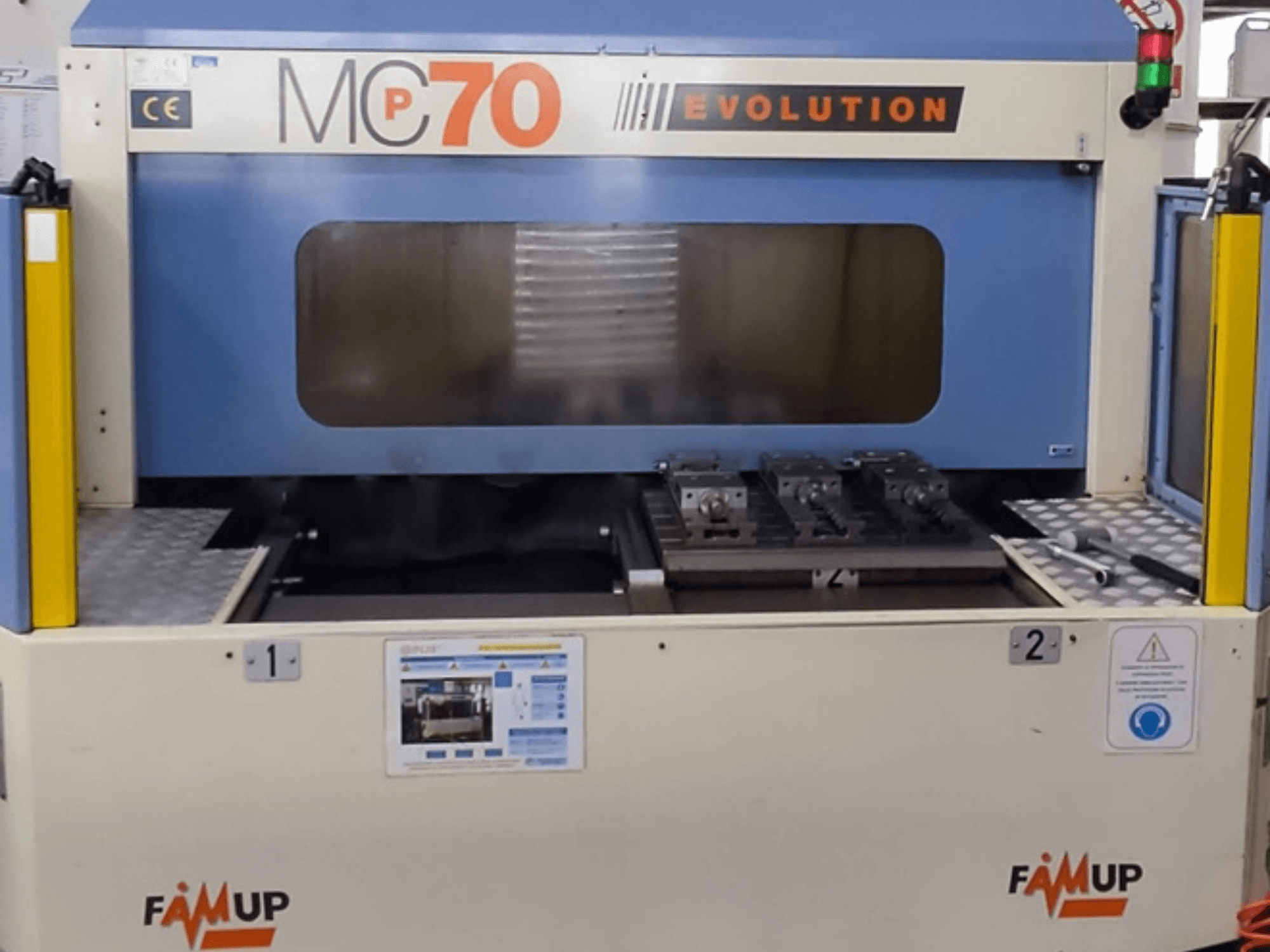 Centre d'usinage vertical FAMUP MCP70 E, vue de face montrant le panneau de commande et la zone de travail avec les dispositifs de fixation et de sécurité.