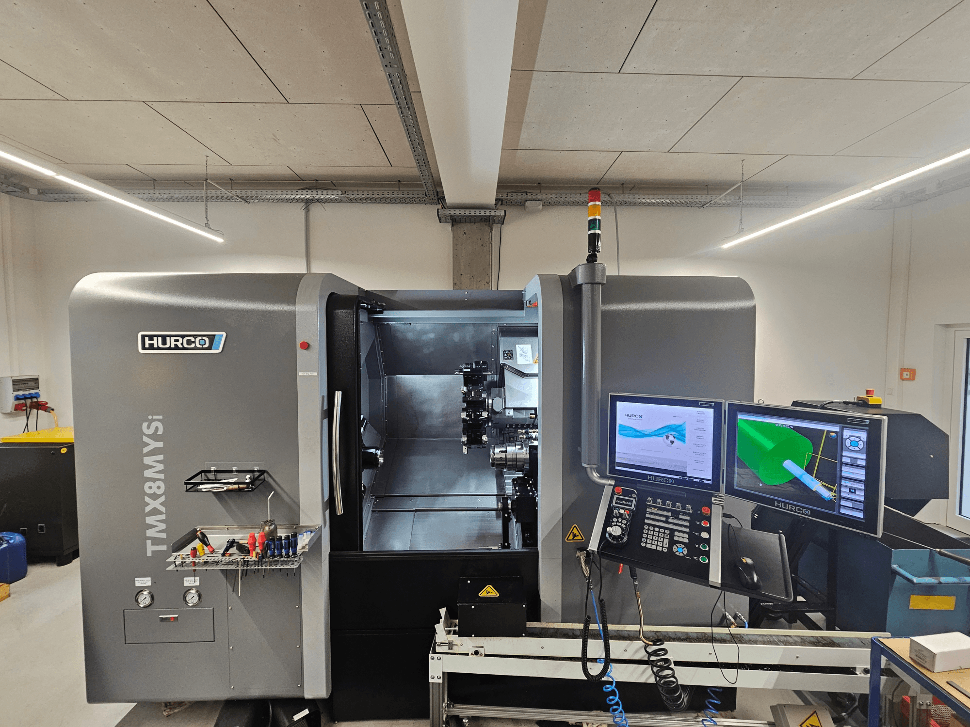 Centre de tournage-fraisage Hurco TMX 8 MYSi dans un atelier, avec deux écrans, un panneau de commande et des outils sur le côté.