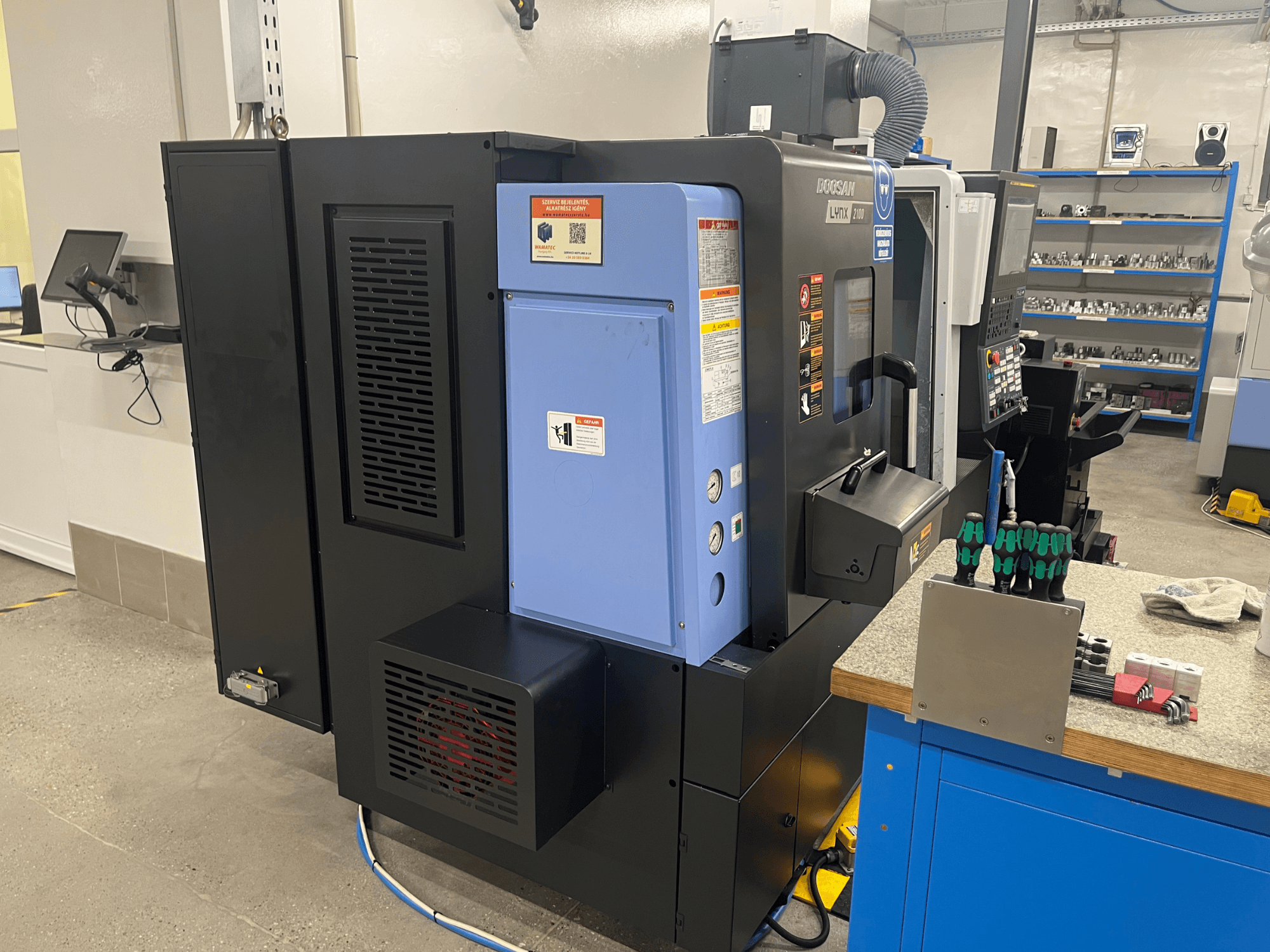 Tour Doosan Lynx 2100, vue latérale, montrant le panneau de commande, le système de ventilation et les outils sur un établi.