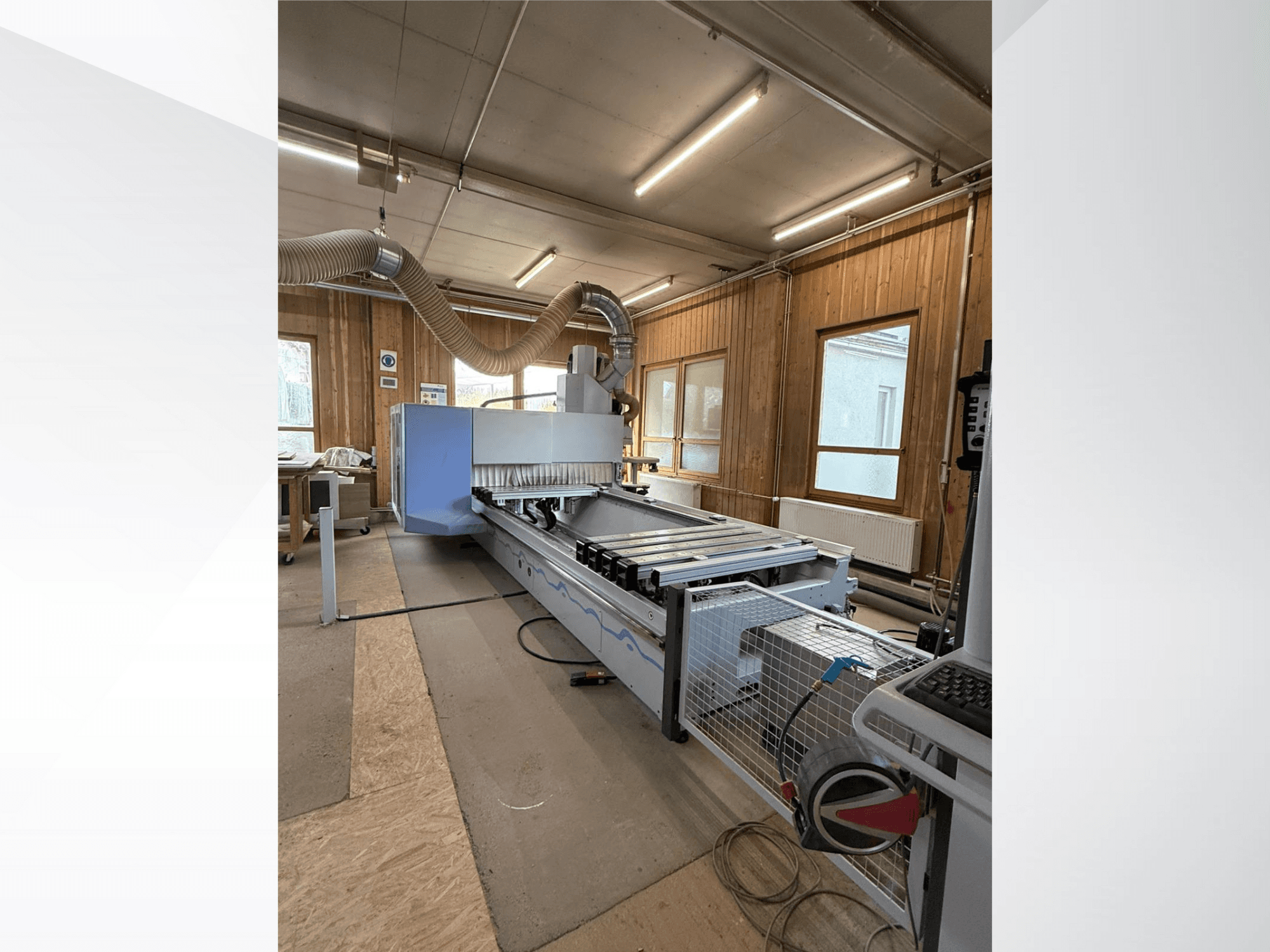 Fraiseuse à commande numérique dans un atelier, vue de côté, avec un grand corps bleu, un convoyeur à bande et un panneau de commande visible.