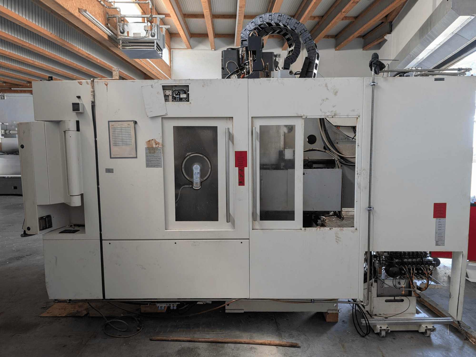 Centre d'usinage vertical STAMA MC 326, vue latérale montrant le panneau de commande, la zone de la broche et diverses étiquettes sur la machine.