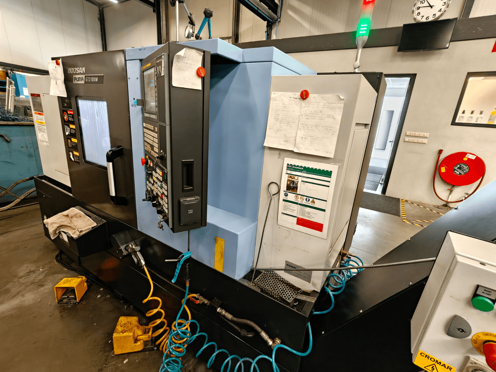 Vue de face du tour horizontal DOOSAN Puma GT 2100M avec le panneau de commande, les dispositifs de sécurité et les notes d'entretien visibles.