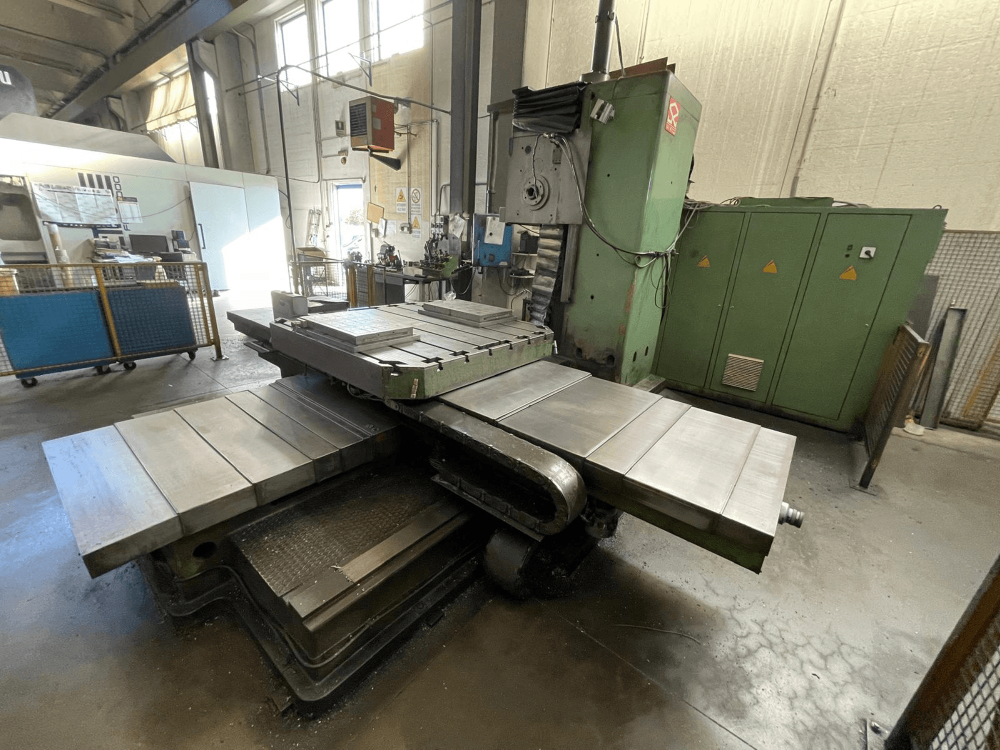 Grande fraiseuse industrielle à carrosserie verte, vue de côté, avec de multiples surfaces planes et des armoires de rangement en arrière-plan.