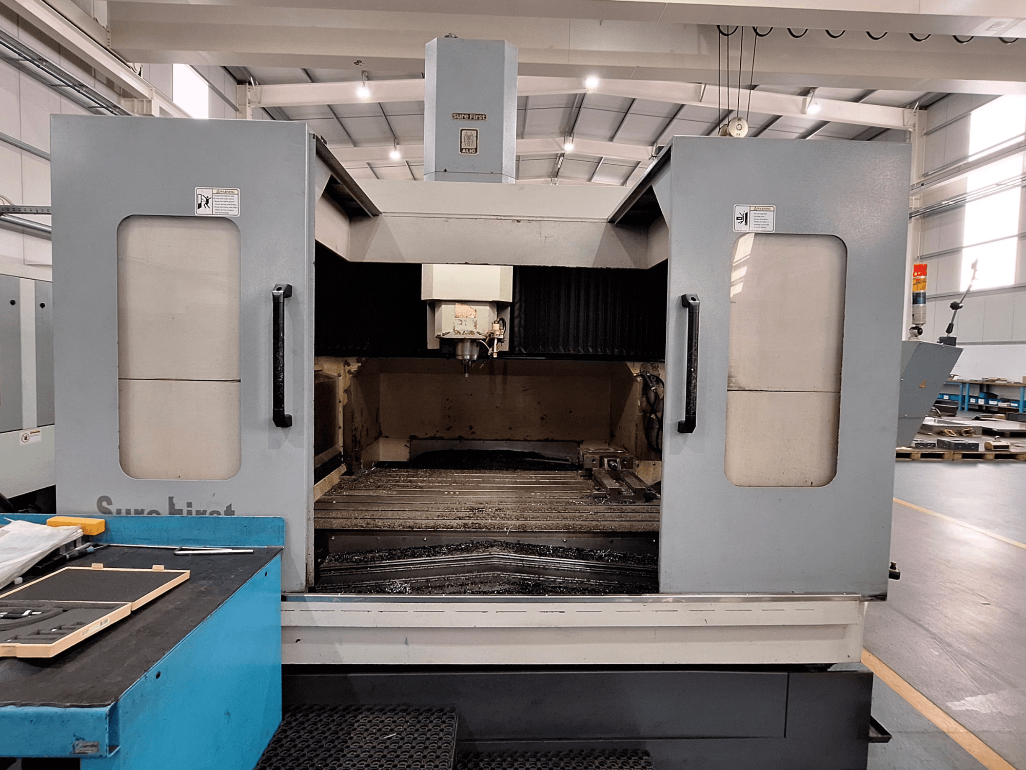 Centre d'usinage vertical Sure First QM-1836, vue de face montrant la tête d'outil et la zone de travail vide, dans un environnement industriel moderne.