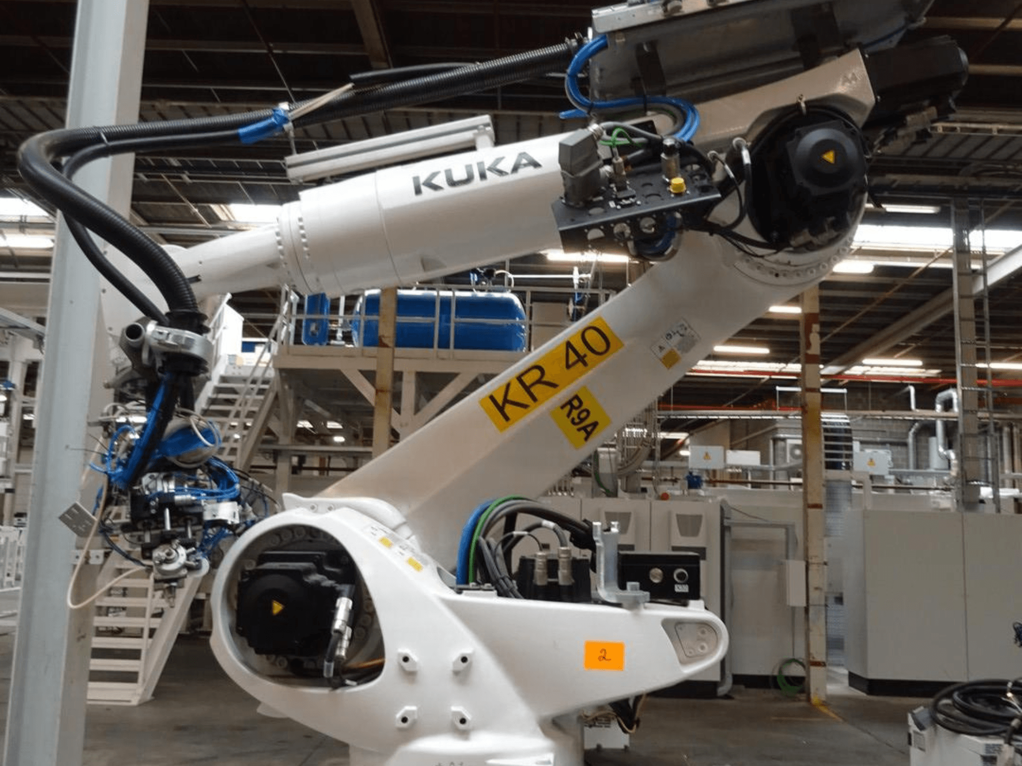 Bras robotique KUKA KR 120 R3100-2 en vue latérale, montrant le panneau de commande et les composants mécaniques, dans un environnement industriel.