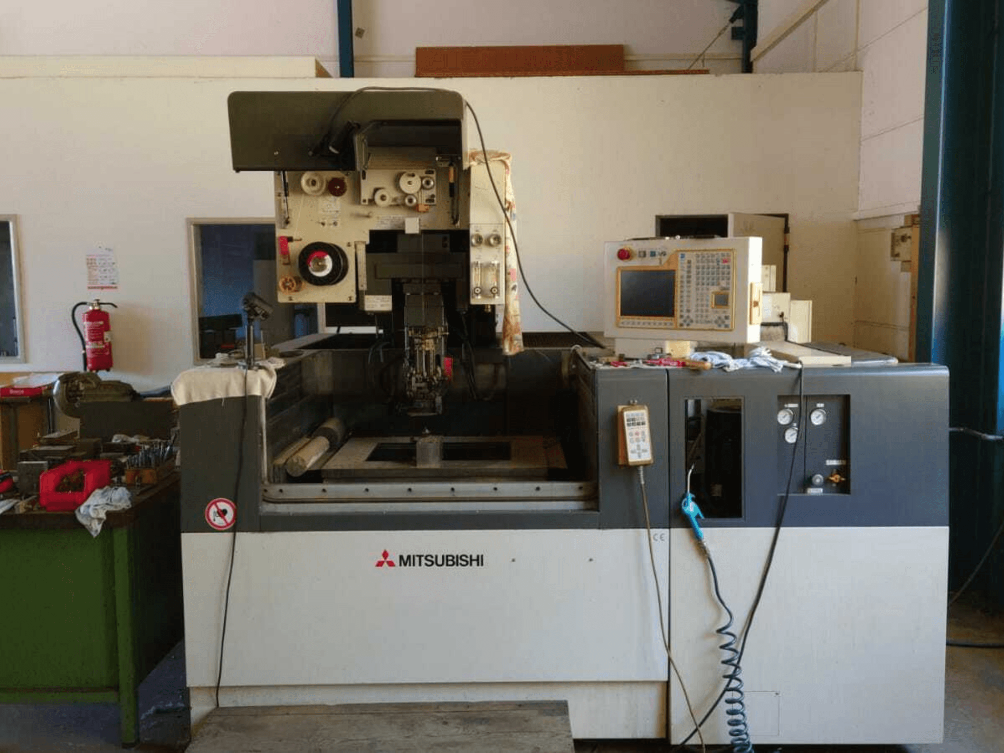 Vue de face de la machine d'électroérosion à fil Mitsubishi FA20, montrant le panneau de commande, la zone de travail et la signalisation de sécurité.