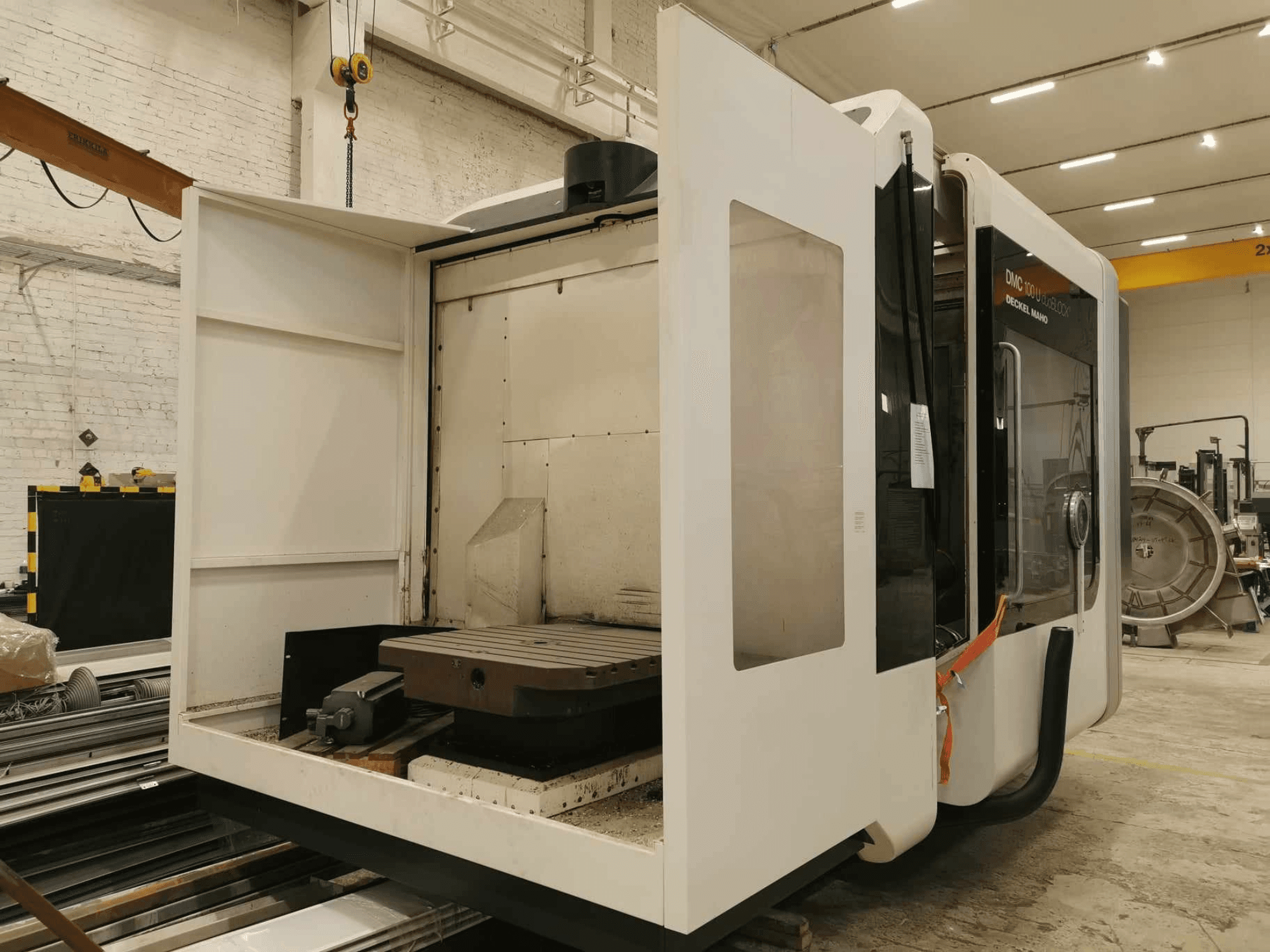 Machine CNC linéaire DMC 100U, vue latérale avec porte d'accès ouverte, montrant la table de travail et les composants internes.