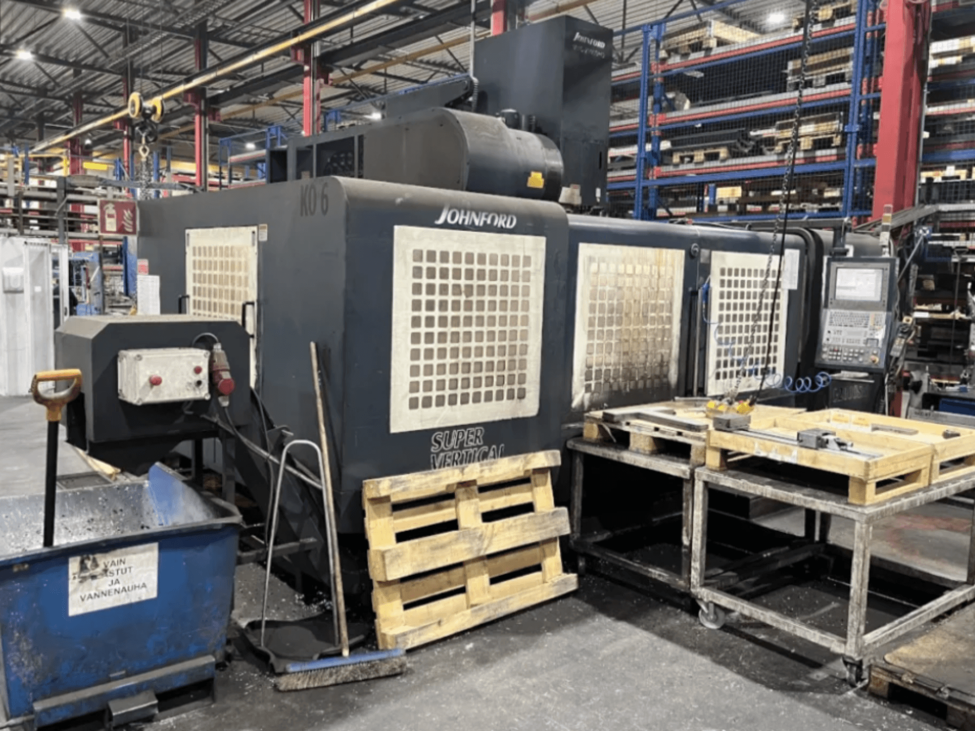 Fraiseuse Johnford Super Vertical dans une usine, vue latérale avec panneau de commande, palettes et équipement de nettoyage à proximité.