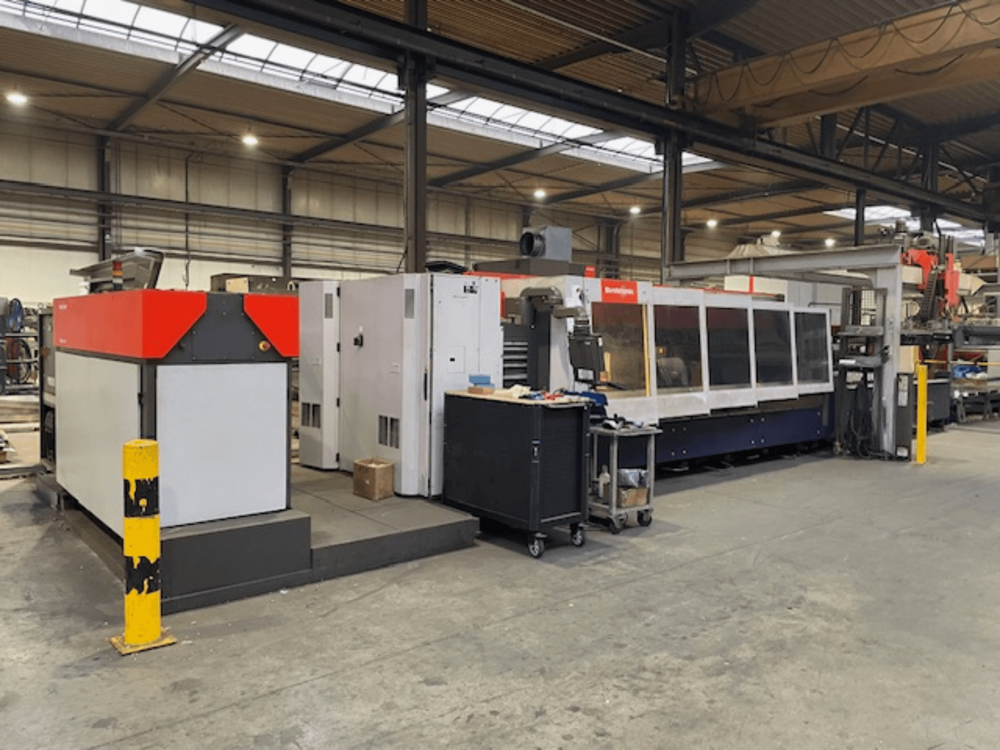 Machine de découpe laser CO2 BySpeed 3015 de Bystronic, vue de côté dans un atelier, présentant des éléments de design rouges et gris distincts.