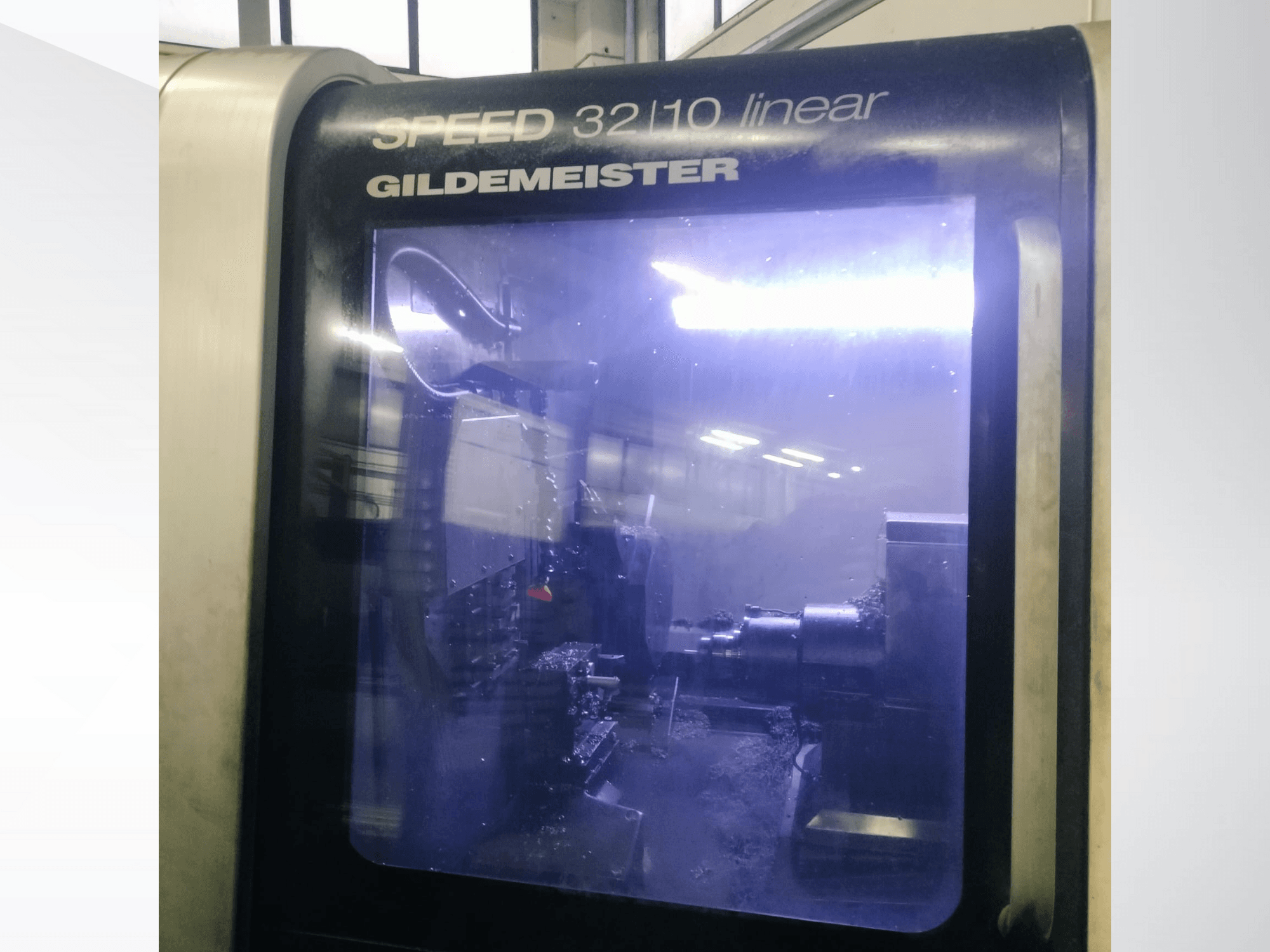 Machine CNC linéaire Gildemeister SPEED 3210 vue de face, montrant les composants internes et le liquide de refroidissement en fonctionnement.
