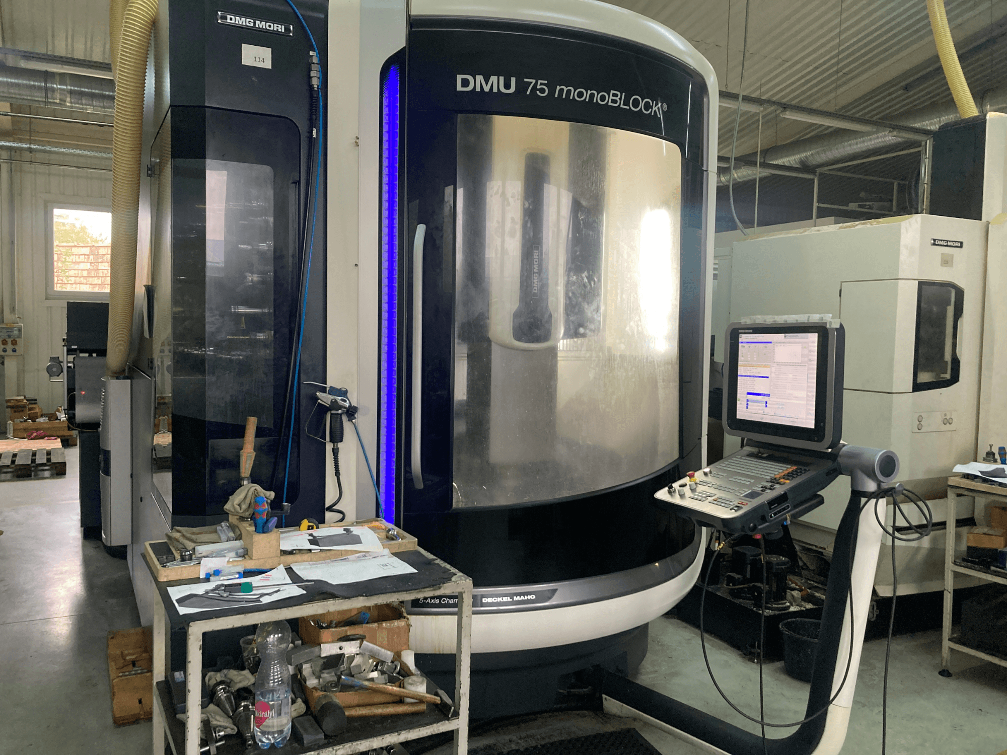 Machine CNC DMG MORI DMU 75 monoBLOCK®, vue de face, avec panneau de commande, outils et espace de travail avec matériaux.