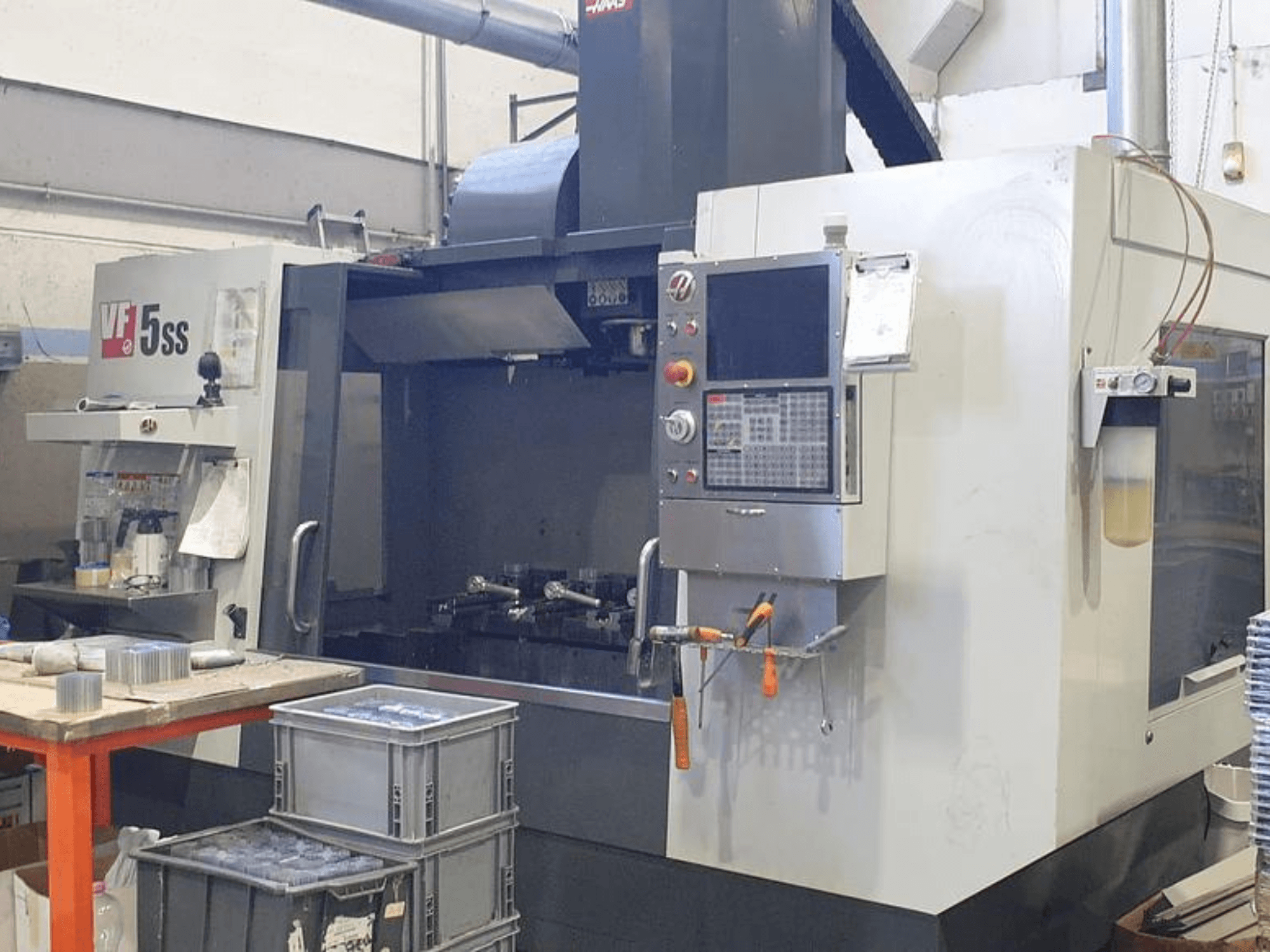 Centre d'usinage vertical HAAS VF-5SS en vue frontale, montrant le panneau de commande, l'espace de travail et les bacs de stockage.