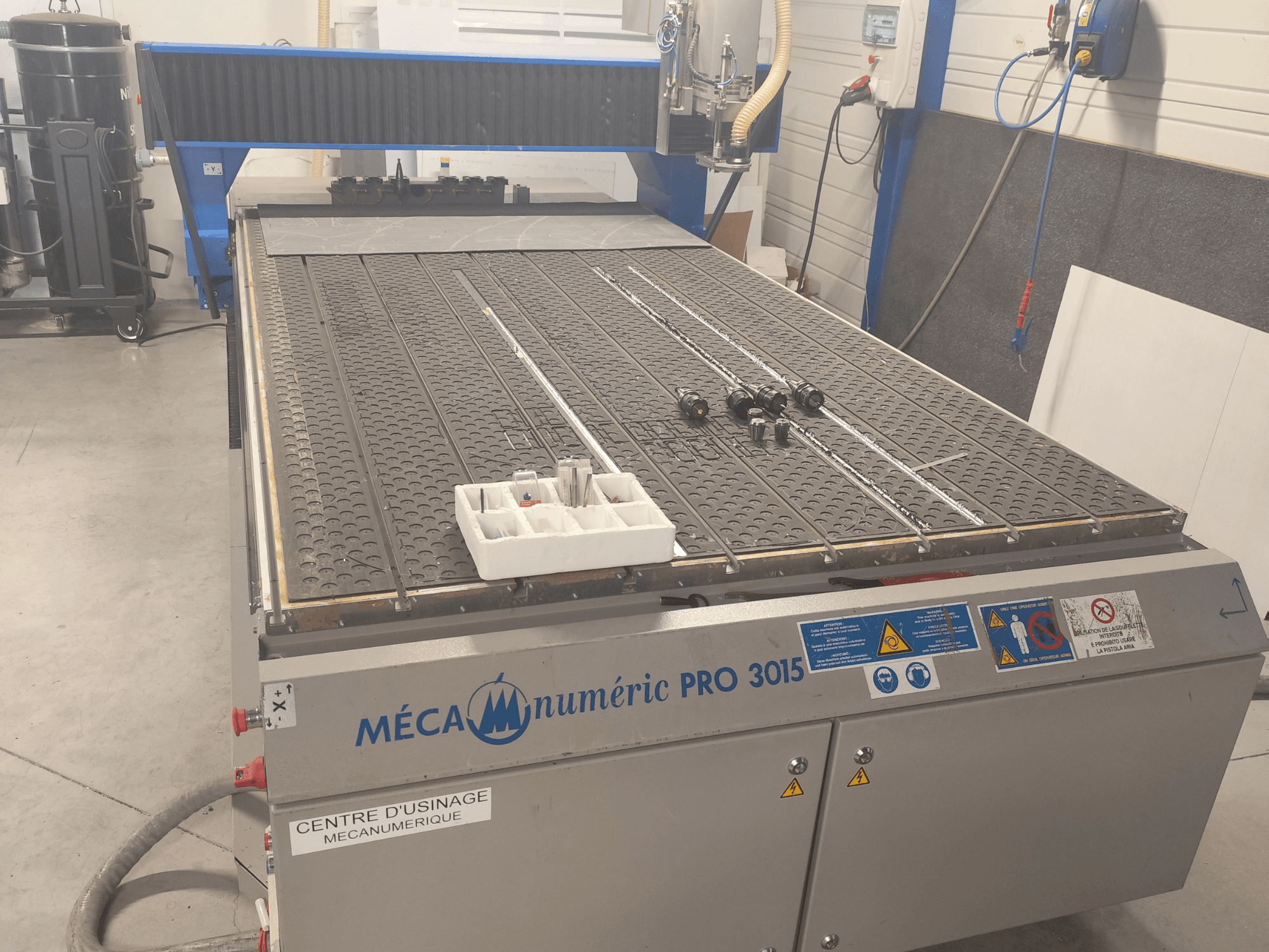 Vue de face de la fraiseuse CNC MECANUMERIC Pro 3015, présentant en détail le plateau de découpe, le panneau de commande et les accessoires posés sur la table.