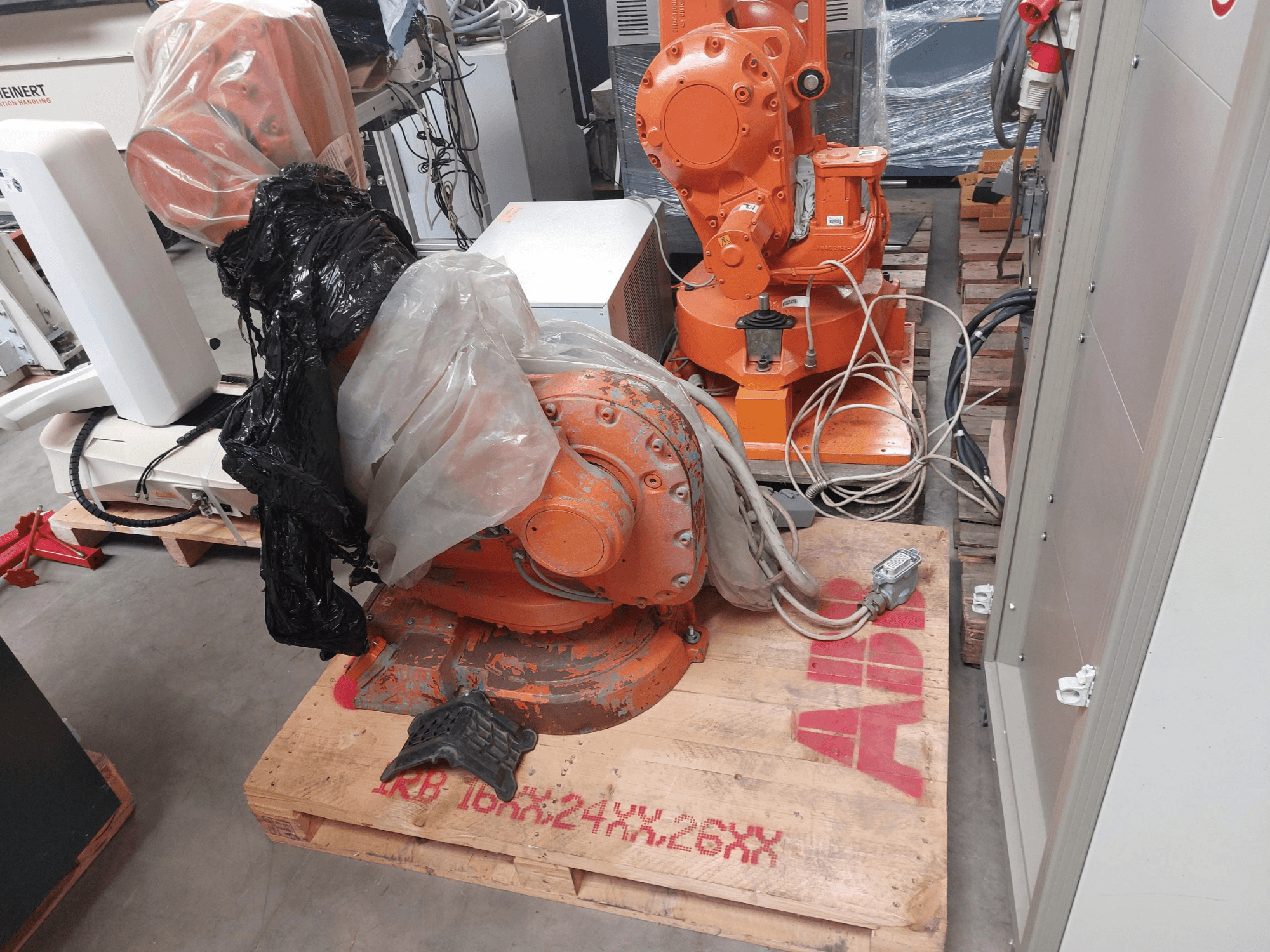 Bras robotique ABB IRB 1600 M2004 partiellement recouvert de plastique, vu de face, avec des câbles et des machines supplémentaires à proximité.