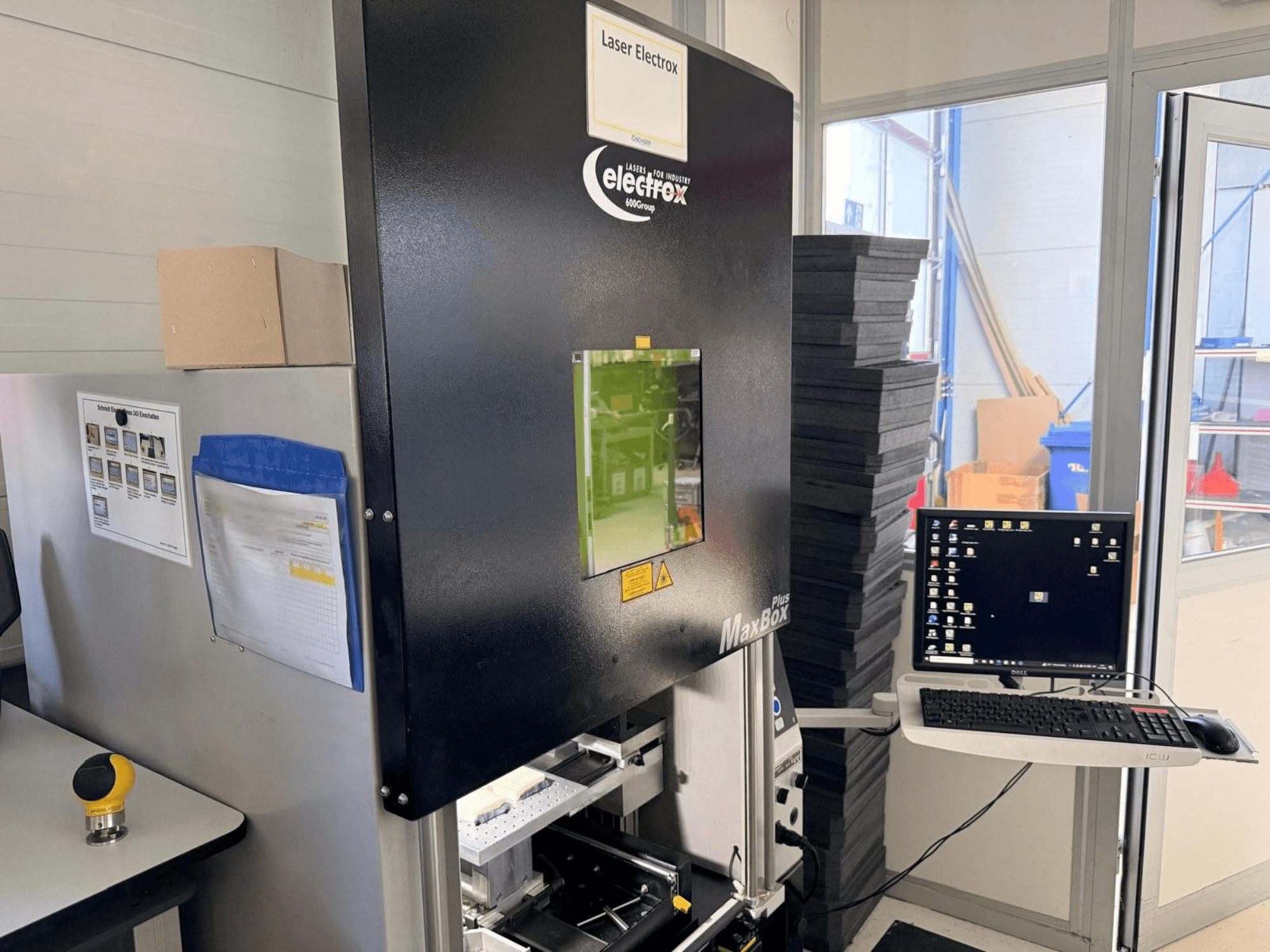 Vue latérale de la machine de marquage laser ELECTROX MaxBox Plus, avec son écran de commande, sa fenêtre de visualisation verte et son espace de travail.
