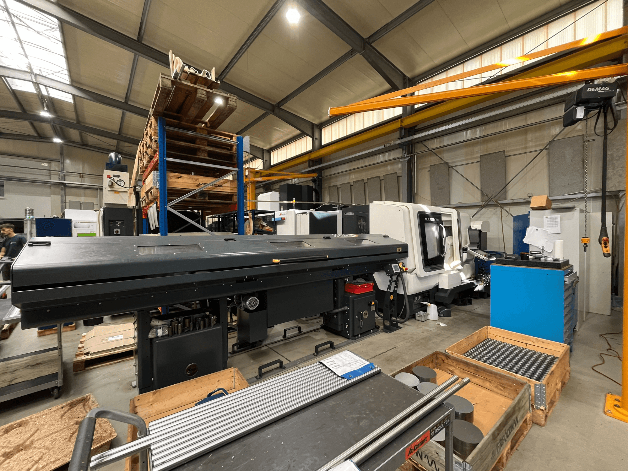 Tour horizontal DMG MORI MORI NLX 2500/700 SY dans un atelier, vu de profil, avec l'espace de stockage et les outils en arrière-plan.
